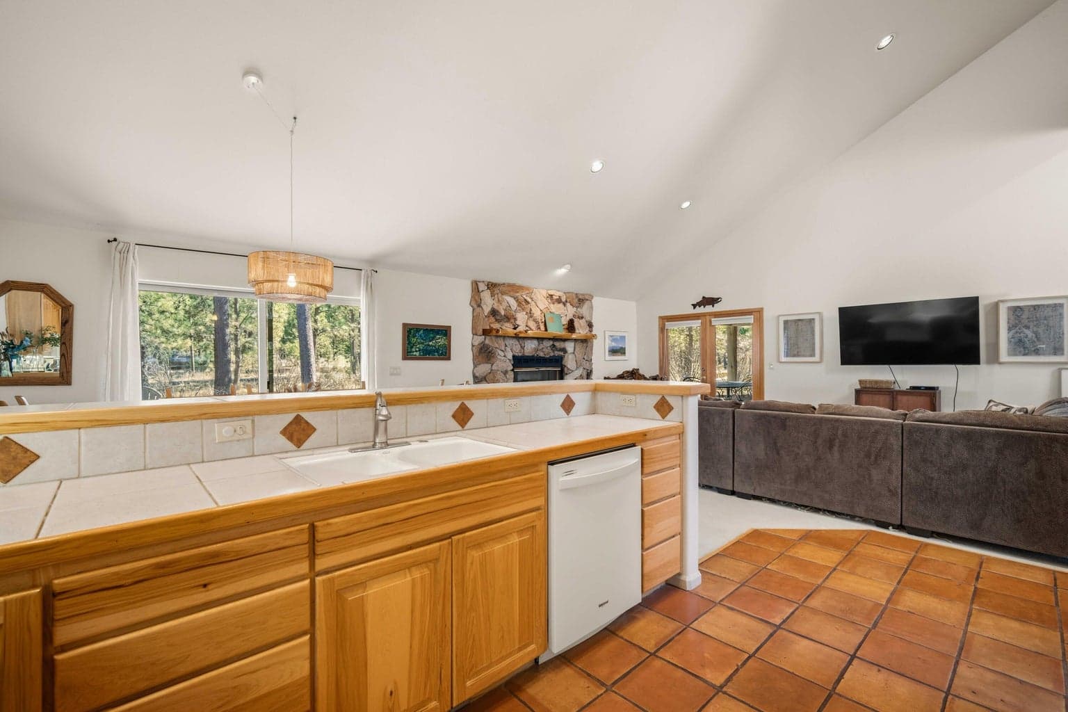 Kitchen view across the great room, showing open-concept living, stone fireplace, and vaulted ceilings.