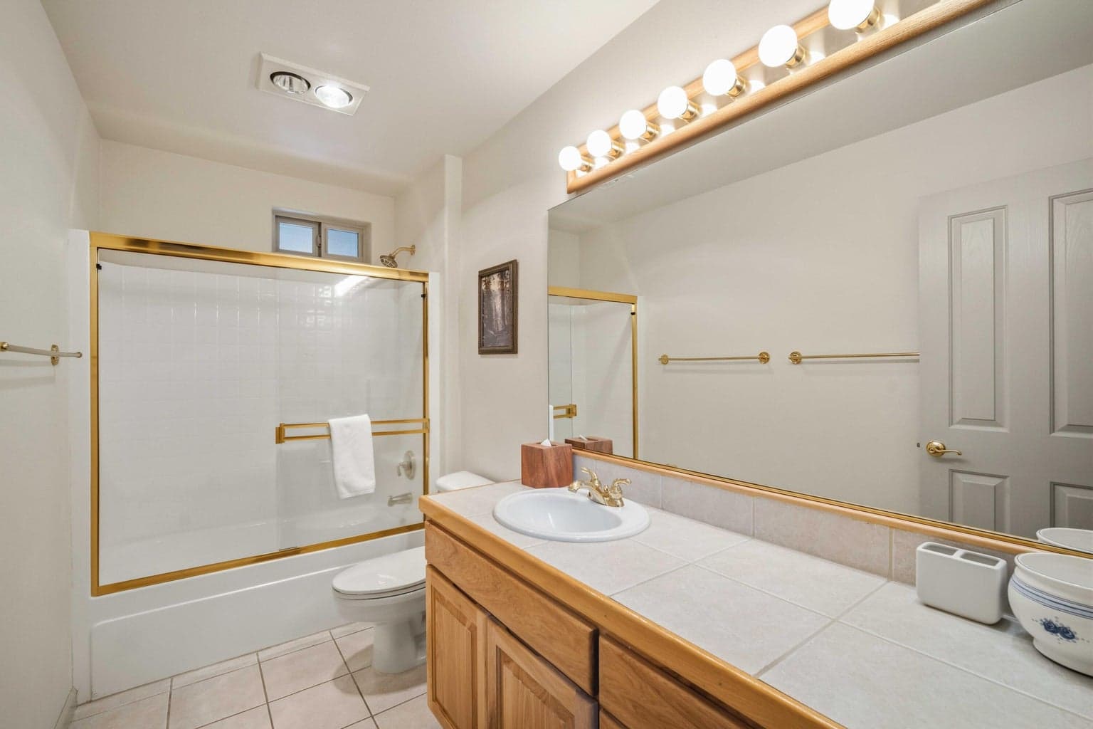 Full bathroom with tub and shower combination, tile counter, and wood vanity near the bedroom wing.