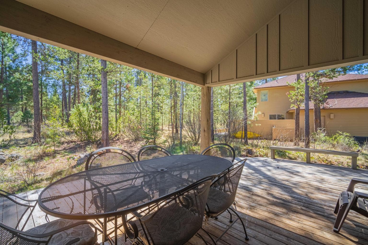 Covered deck with outdoor dining and views into the surrounding trees and natural Central Oregon landscape.
