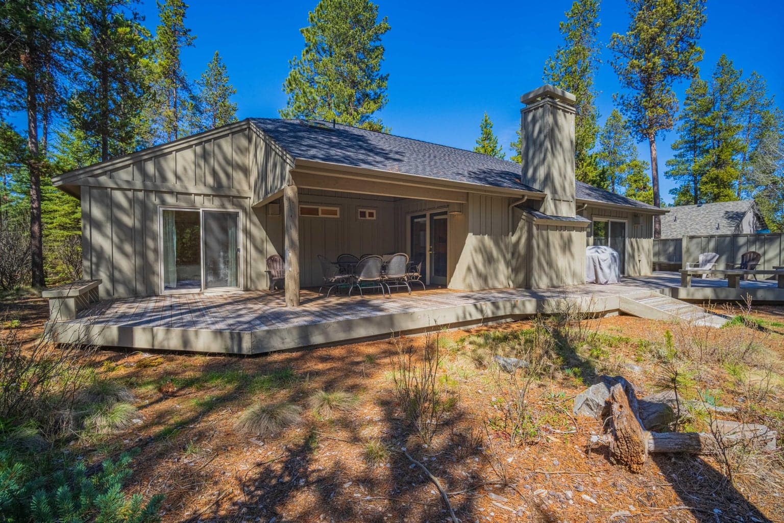 Rear exterior of the home with expansive decking, covered dining, open seating, and natural landscaping.