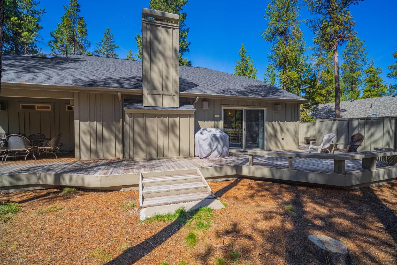 Back deck view with central chimney, outdoor seating zones, and mature trees framing the property.