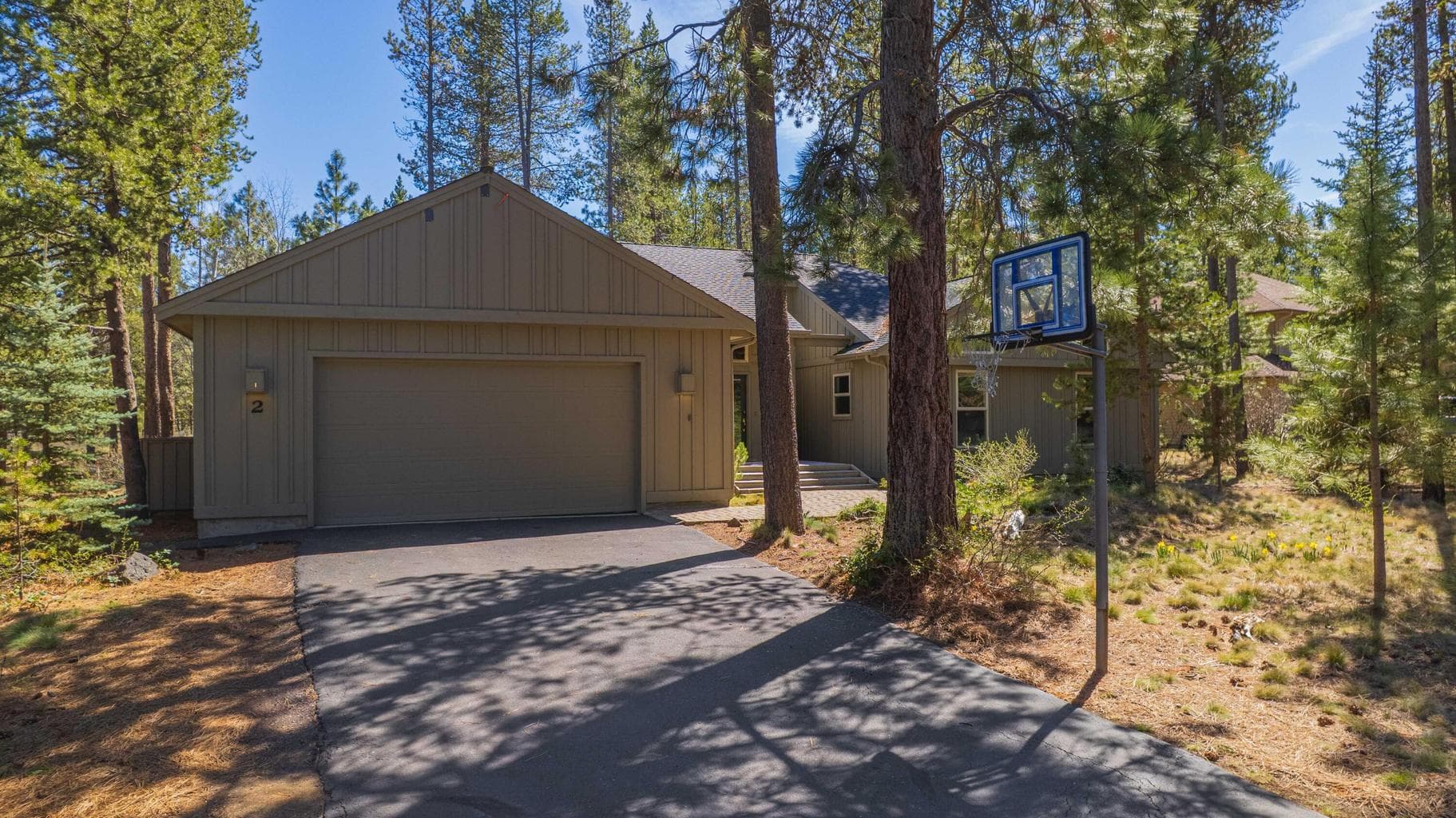 Driveway and garage approach with basketball hoop, native vegetation, and a quiet Sunriver neighborhood feel.