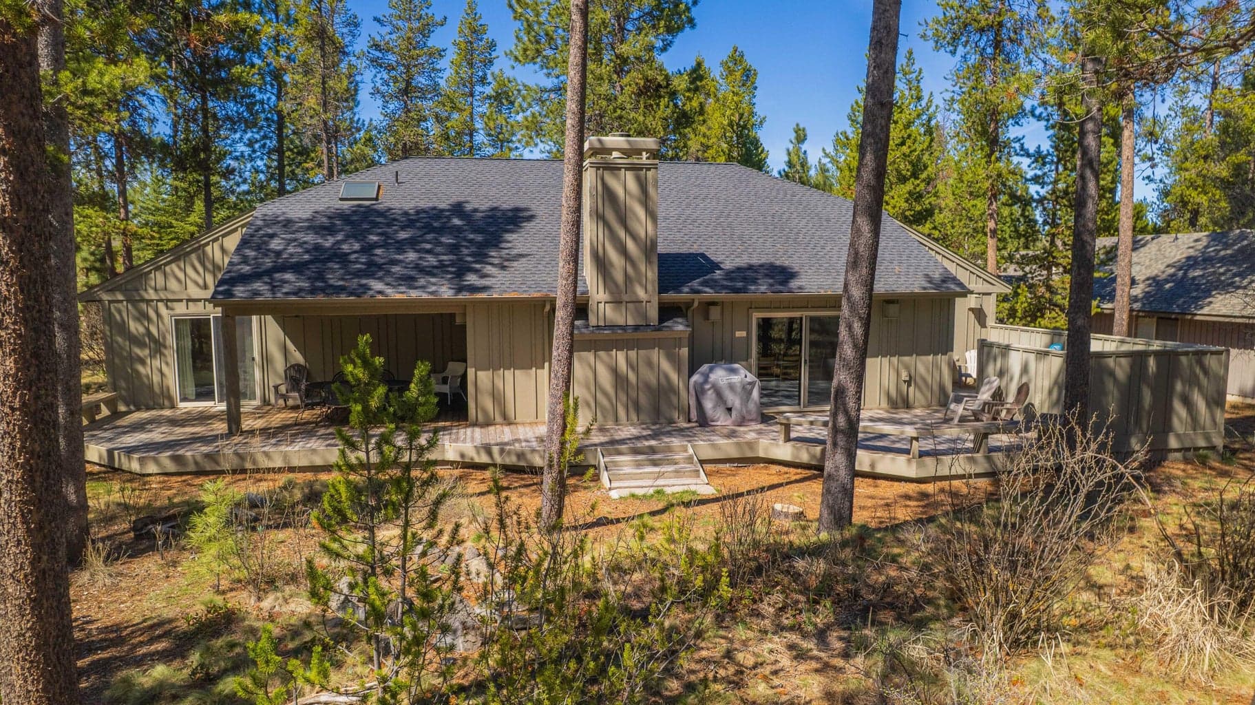 Rear view from the natural pine setting, showing the home’s broad deck and connection to the surrounding landscape.