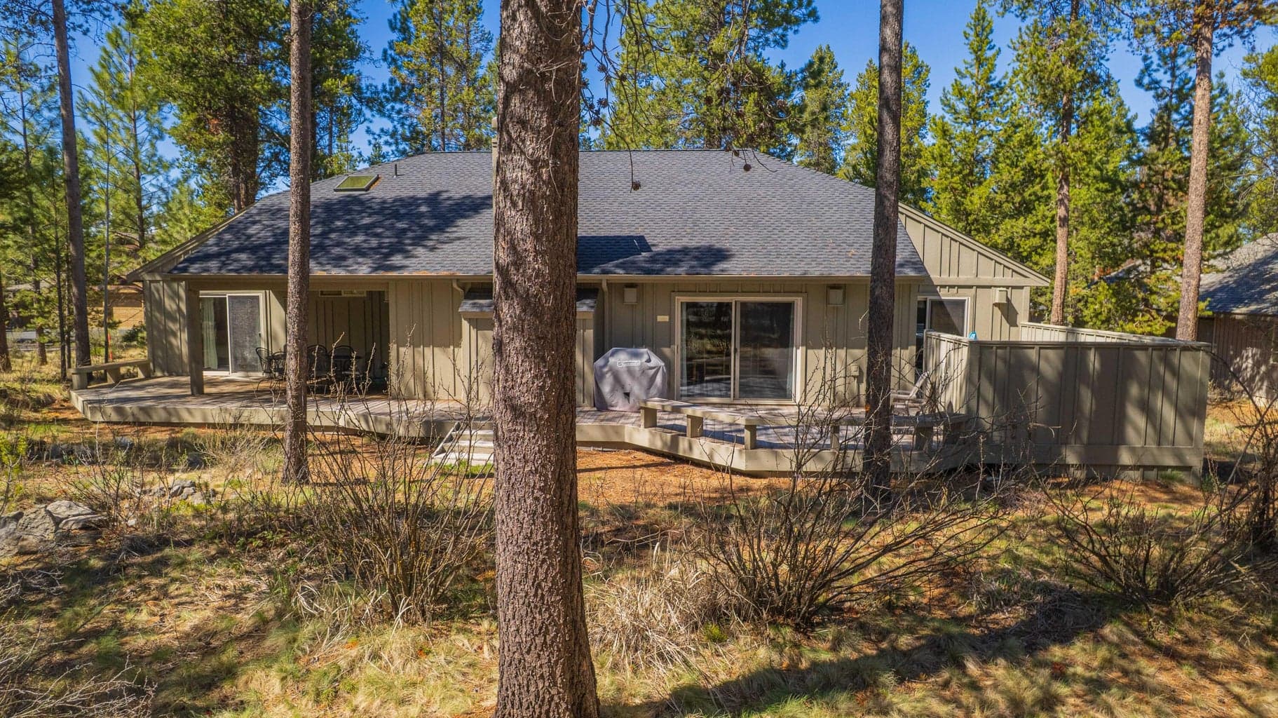 Wide rear exterior view with mature trees, expansive decking, and a peaceful North Sunriver setting.
