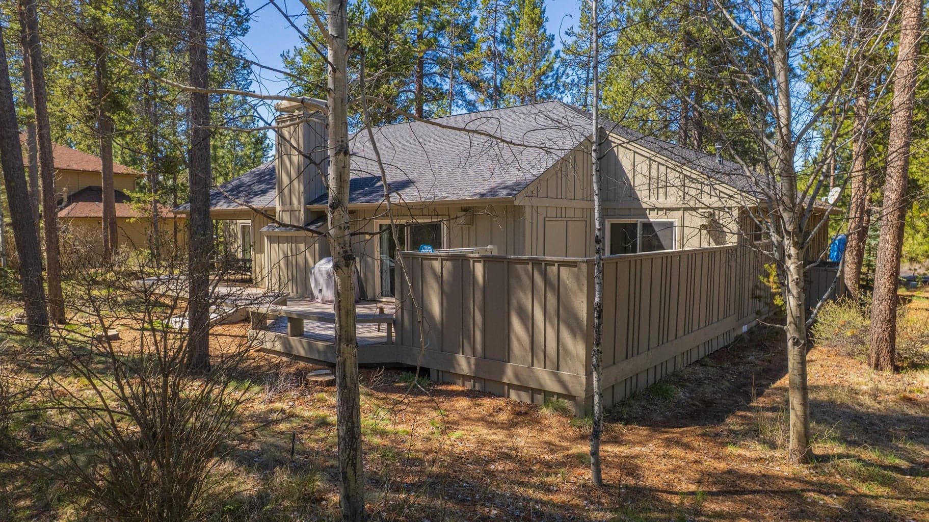 Side and rear exterior view showing the fenced hot tub area, deck layout, and natural Sunriver surroundings.