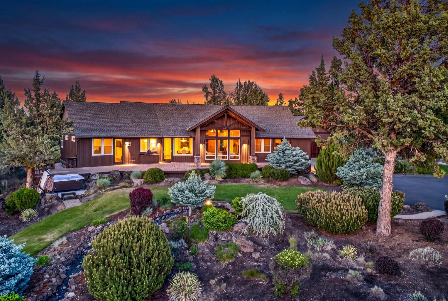 The custom PacWest-built single-level residence glows at sunset, surrounded by mature landscaping, outdoor living areas and a sweeping Cascade Mountain-view setting.