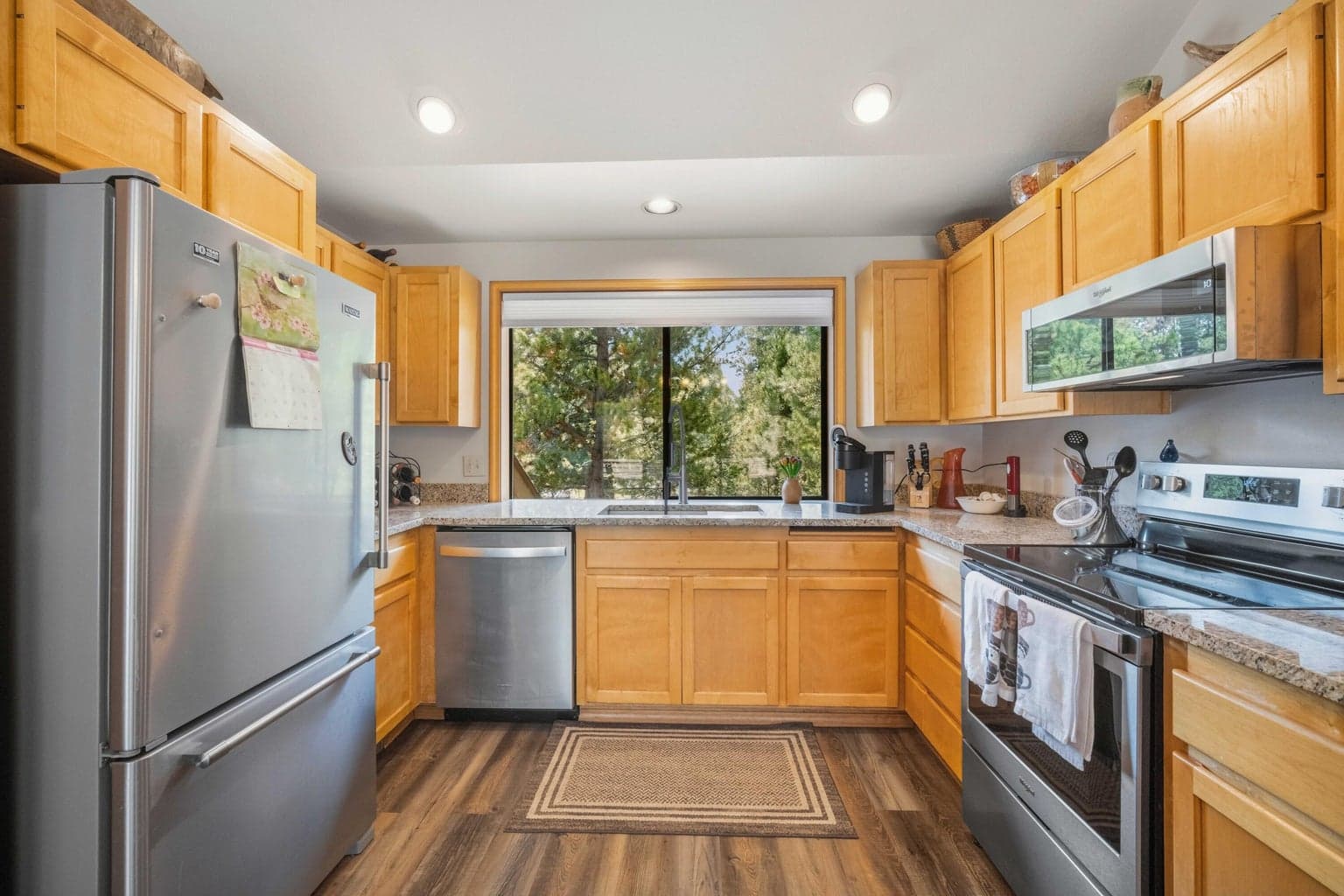 Kitchen work area with stainless appliances, updated countertops, and windowed tree views.