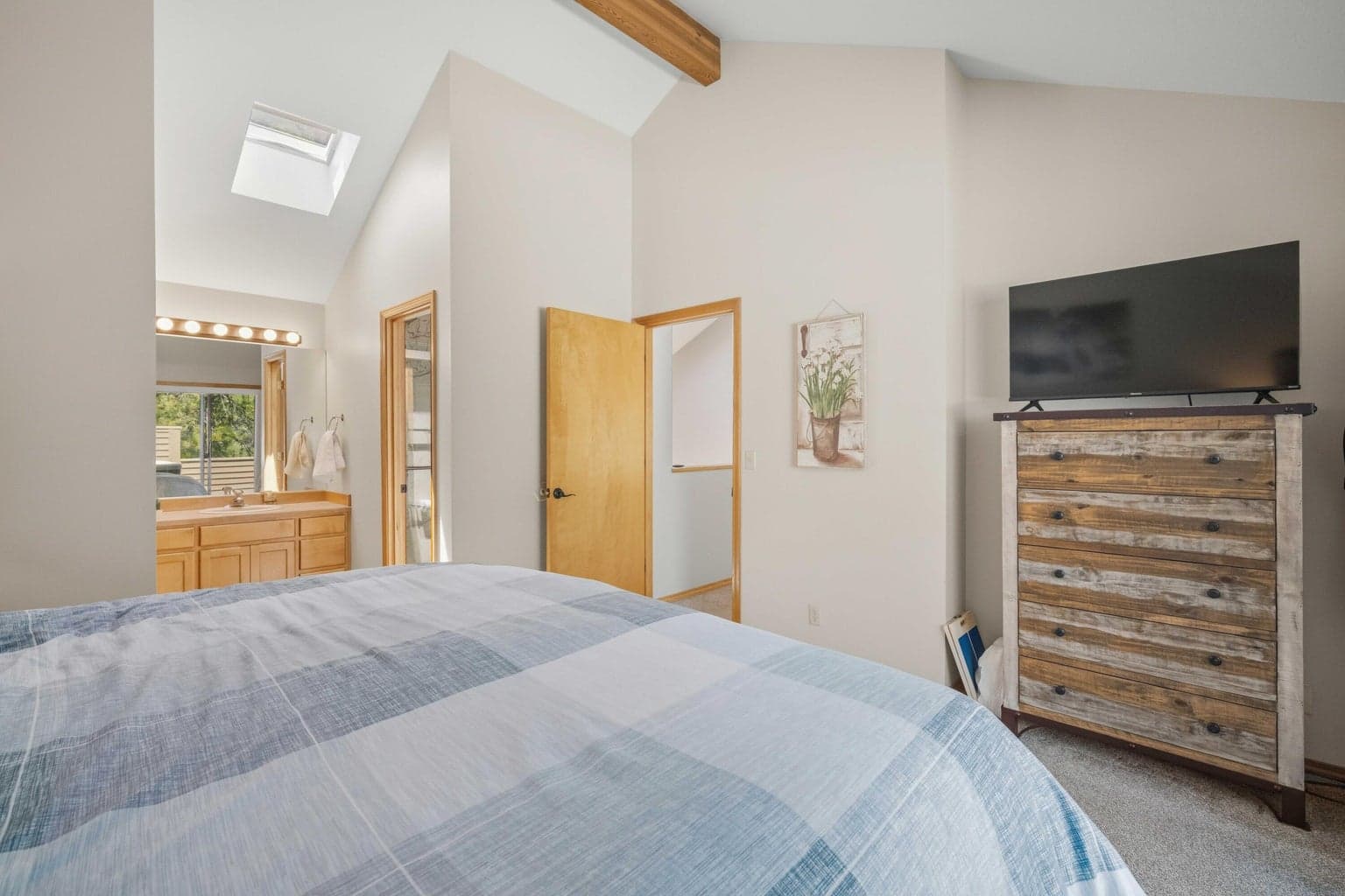 Bright primary bedroom with vaulted ceiling, skylight, and warm natural trim.