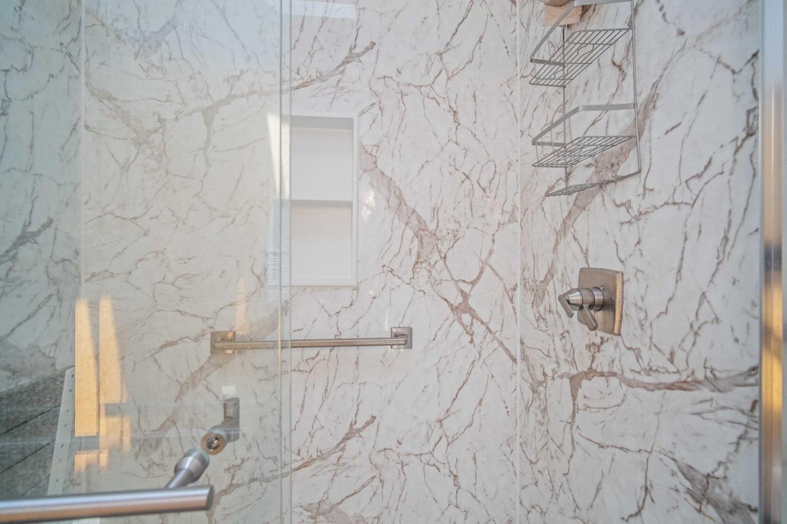 Updated primary walk-in shower with glass door and marble-look surround.
