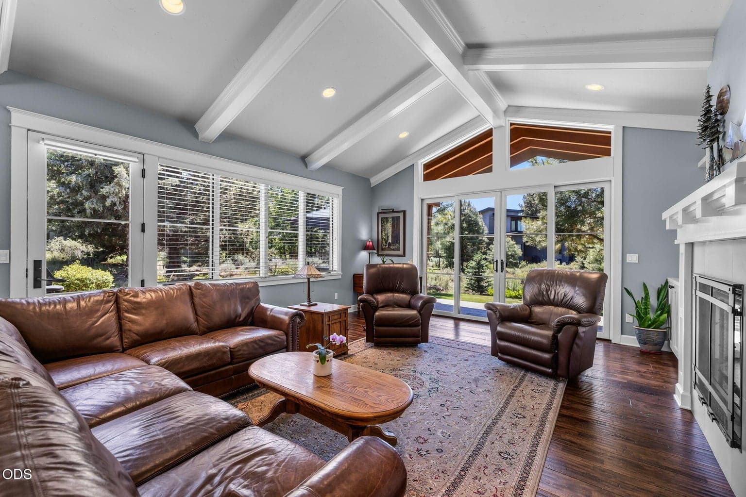 Vaulted great room with architectural ceiling detail, fireplace, built-ins, rich wood flooring, and walls of glass opening to the outdoors.