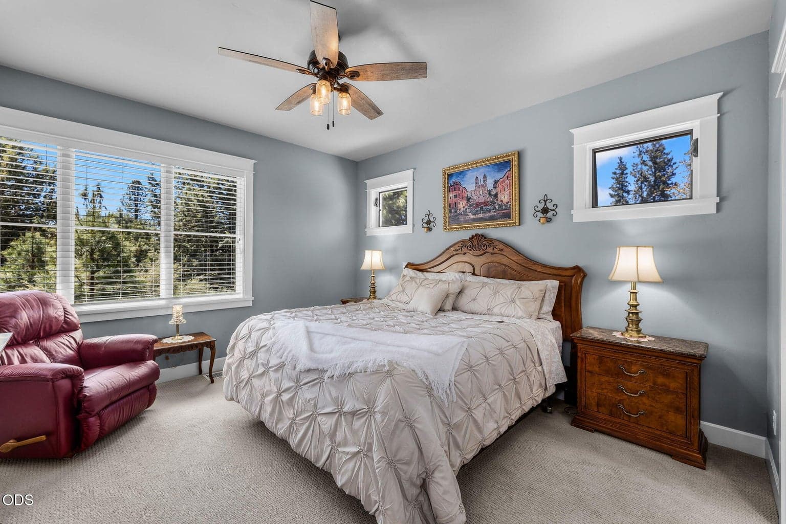 Spacious main-level primary suite with soft natural light, generous windows, and a peaceful view toward the landscaped setting.