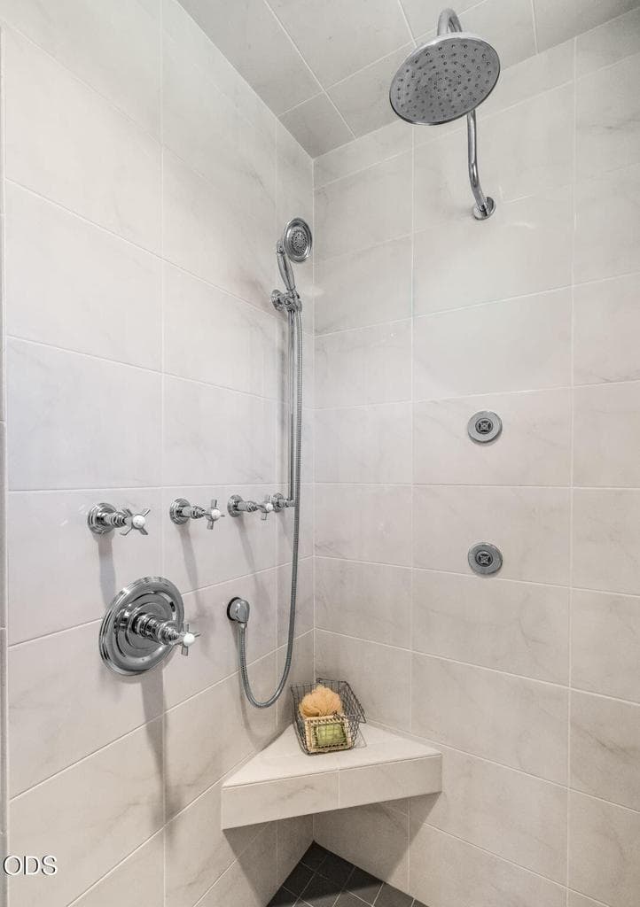 Large tiled shower with rain shower head, handheld fixture, body sprays, and built-in bench for a true spa-like experience.