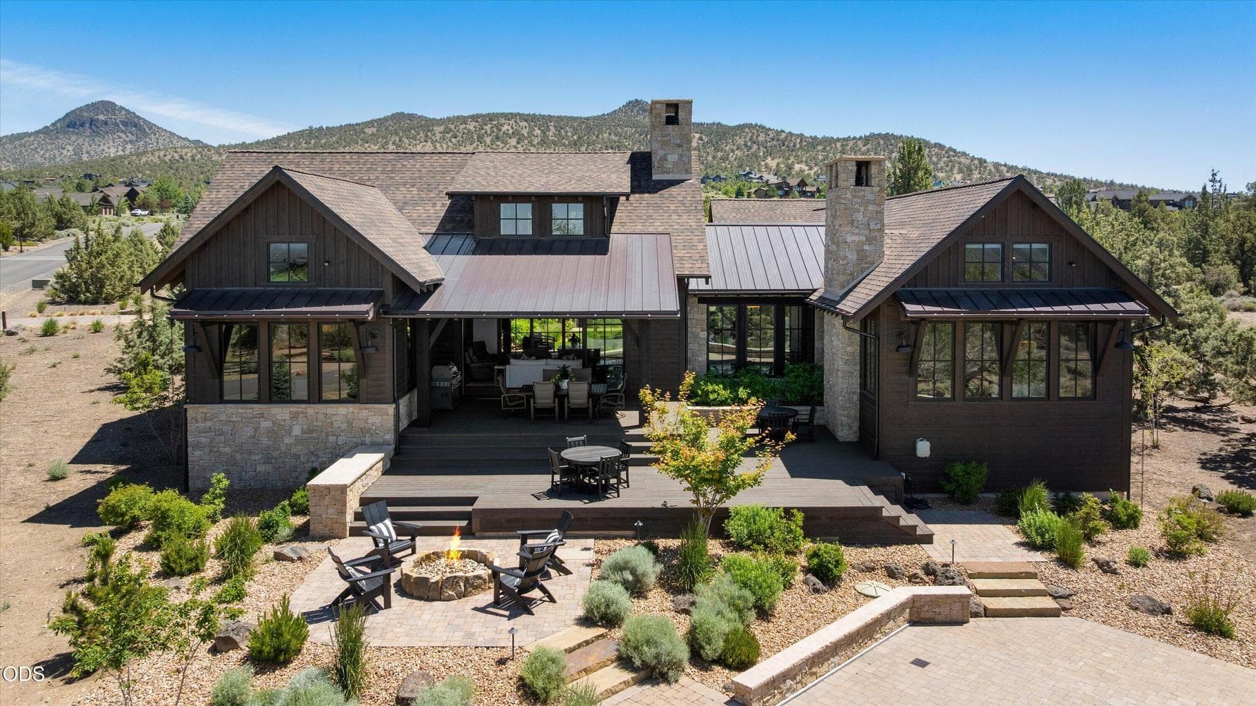 Back of home showing landscaping, gas firepit, paved pool deck, and wood decks