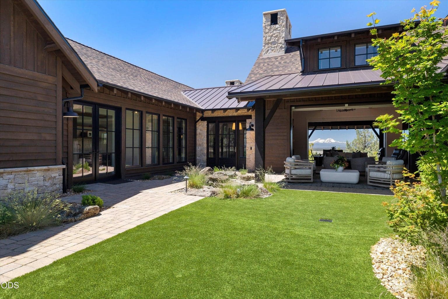 Courtyard featuring pavers, easy landscape, covered patio, views through the home to the mountains beyond, tranquil Montana Moss rock water feature, and doors to the guest suites