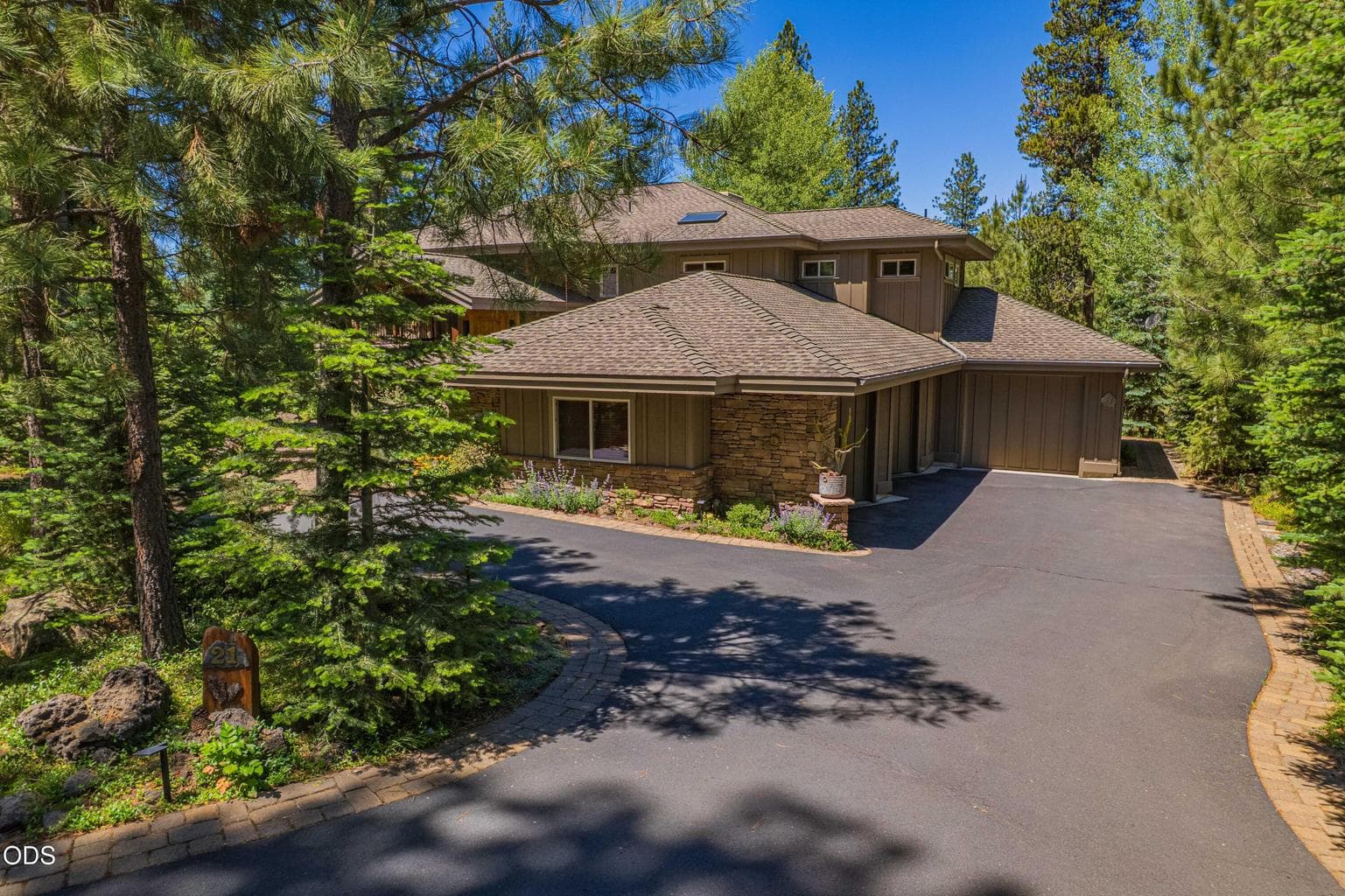 Impeccably maintained Sun Forest-built home with an attached three-car garage, stone detailing, generous paved parking, and a private Sunriver setting surrounded by mature trees.