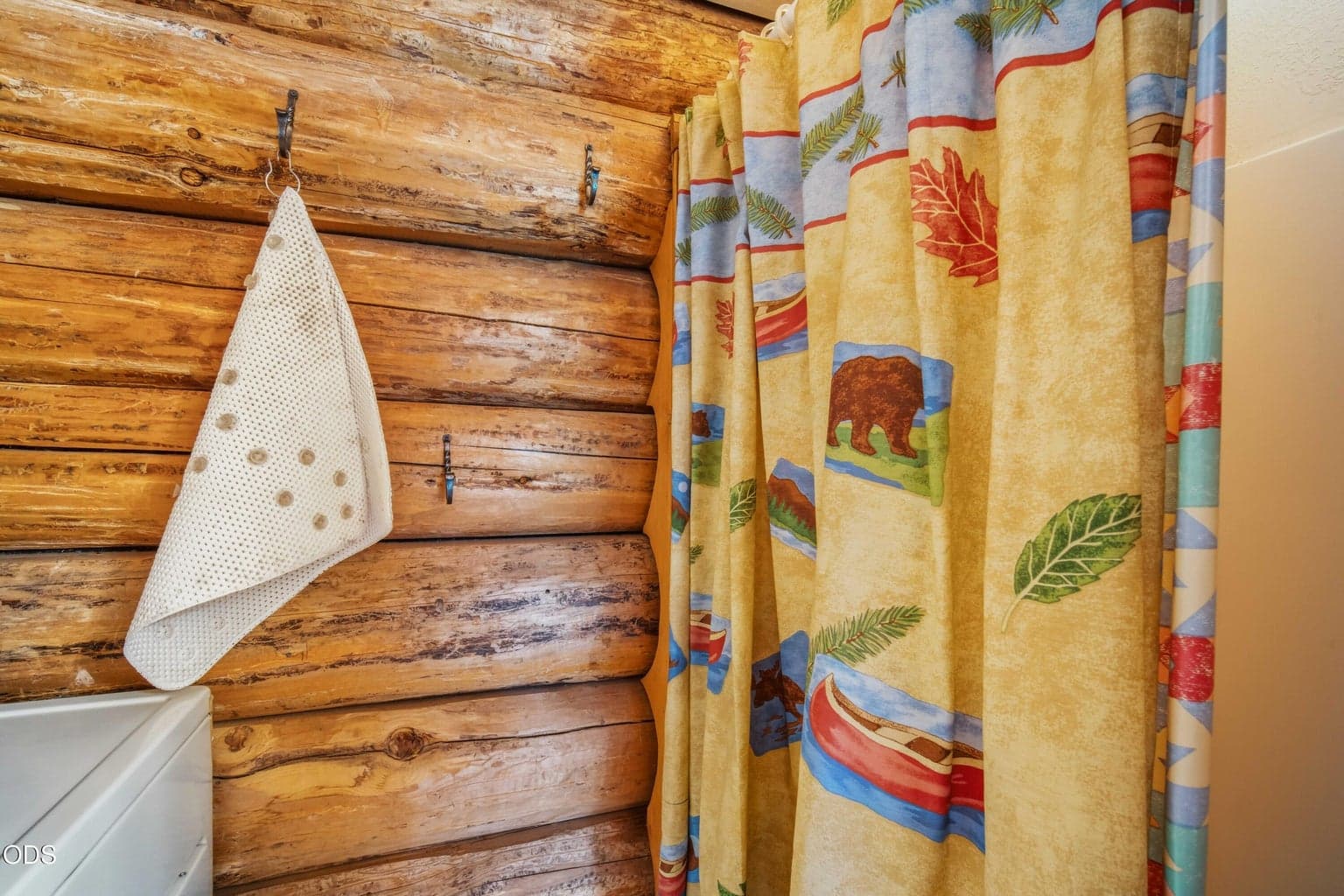 The shower and laundry area combine everyday function with the cabin’s warm log-wall detailing.
