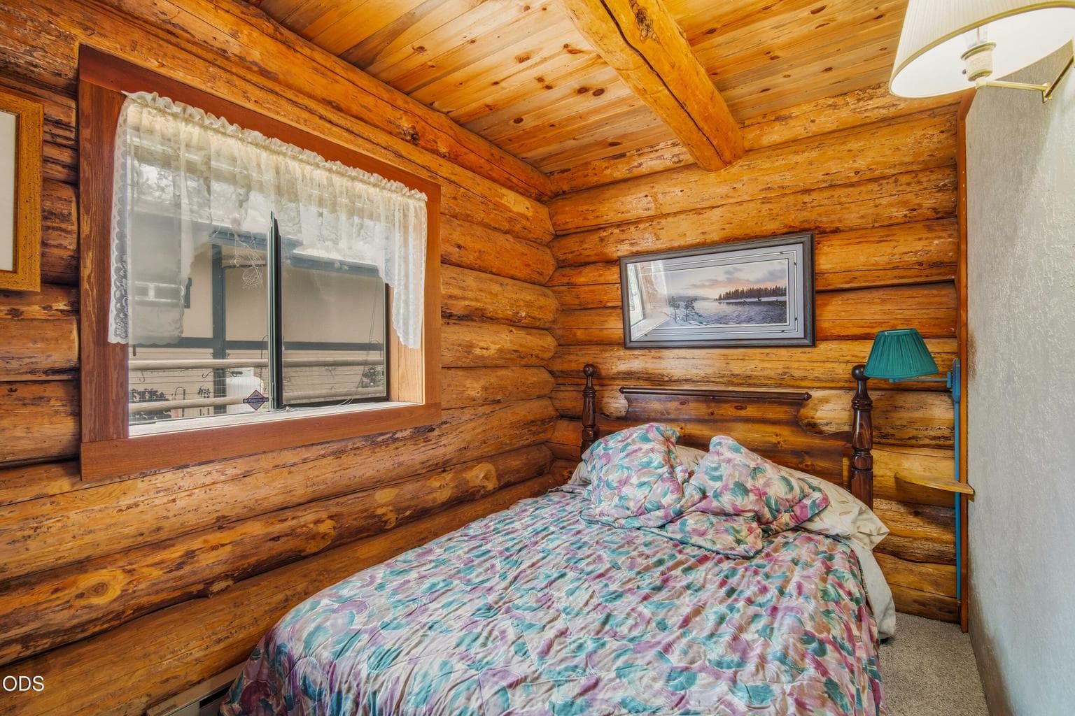 The main-level bedroom offers warm log walls, a wood ceiling, and a cozy place to settle in after a day outdoors.