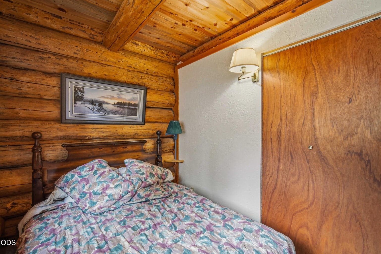 A second view of the main-level bedroom shows its warm log construction and practical closet storage.