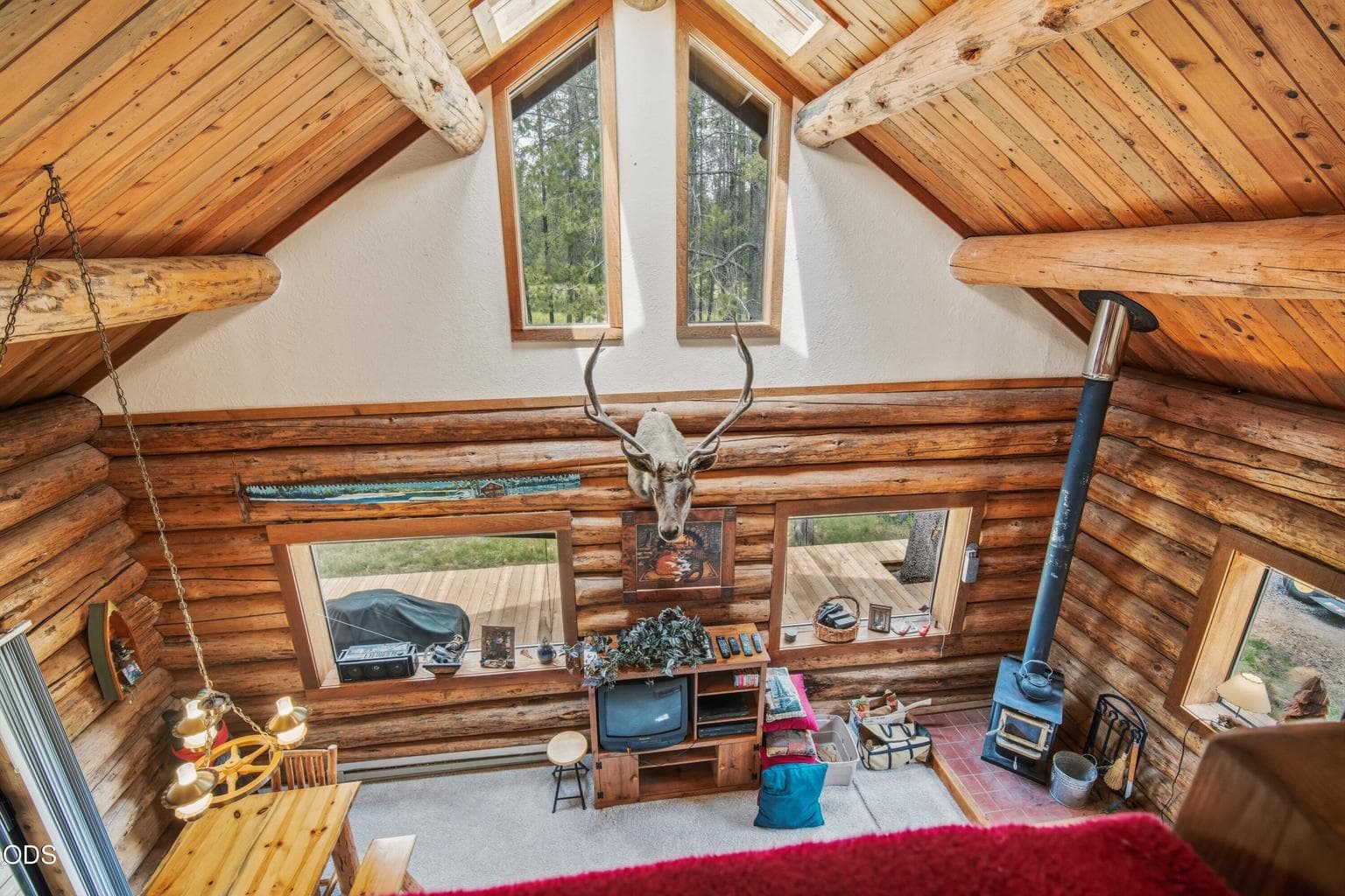From the loft, the vaulted great room, wood stove, tall windows, and log walls come together in one dramatic view.