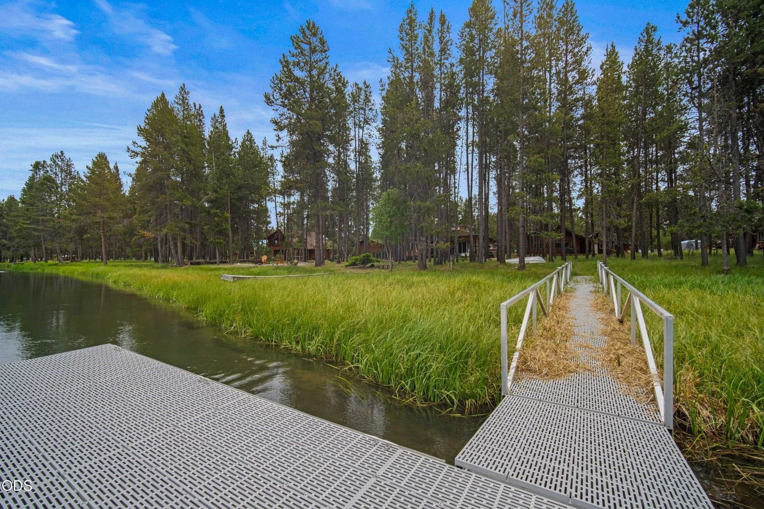 Looking back from the river, the dock and walkway lead through the grasses and trees toward the secluded log cabin setting.
