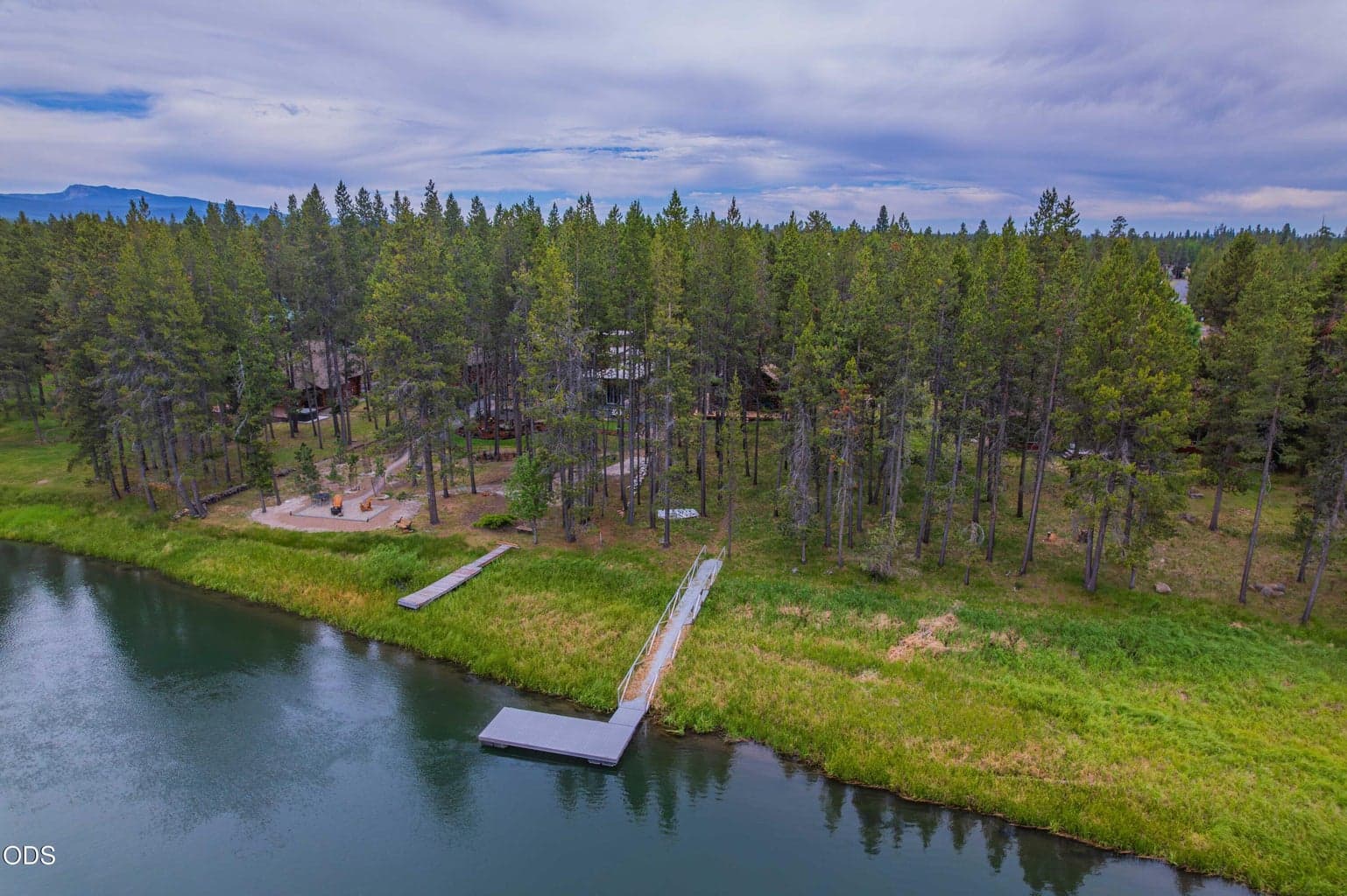 55915 Wood Duck Drive offers a peaceful Big Deschutes River setting with a classic log cabin, shared dock, wooded .68-acre lot, and separate permitted guest bedroom and bathroom space in Bend, Oregon.