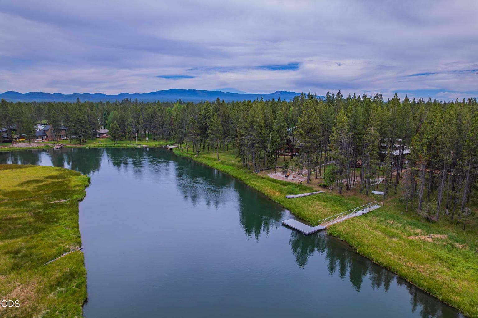 An aerial perspective reveals the property’s relationship to the Big Deschutes River, dock, natural shoreline, and surrounding Central Oregon forest.