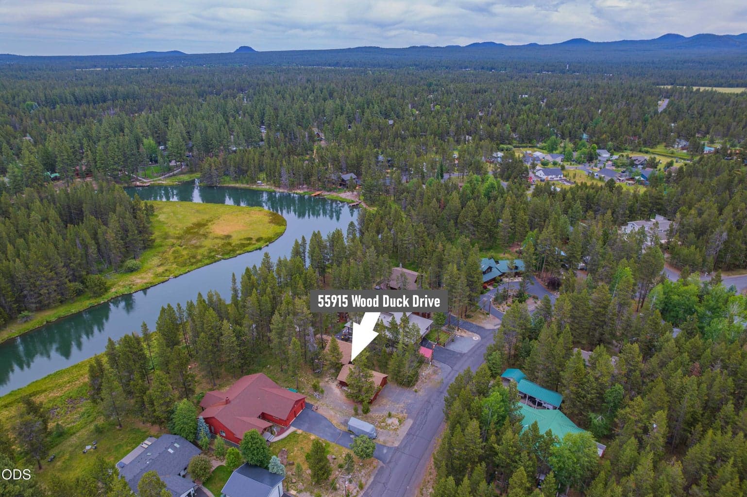 The final aerial captures the full Central Oregon setting of 55915 Wood Duck Drive, where the Big Deschutes River, wooded neighborhood, and Cascade horizon come together.