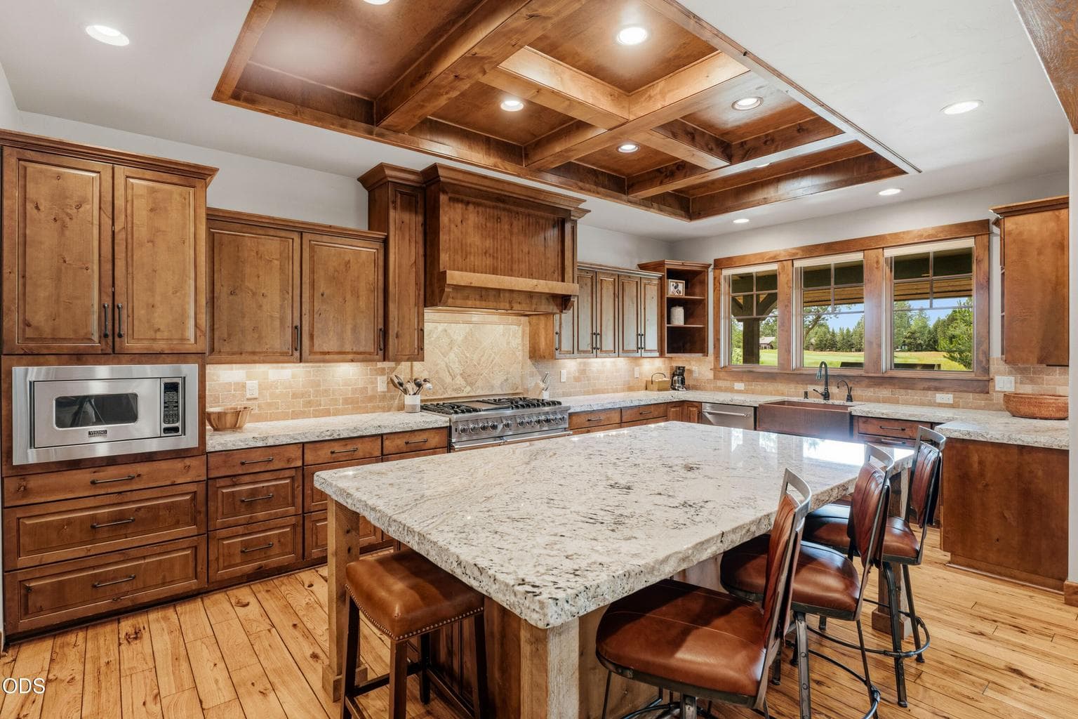 A spacious granite island with seating, coffered wood ceiling, and abundant custom cabinetry creates the perfect gathering space for family and friends.