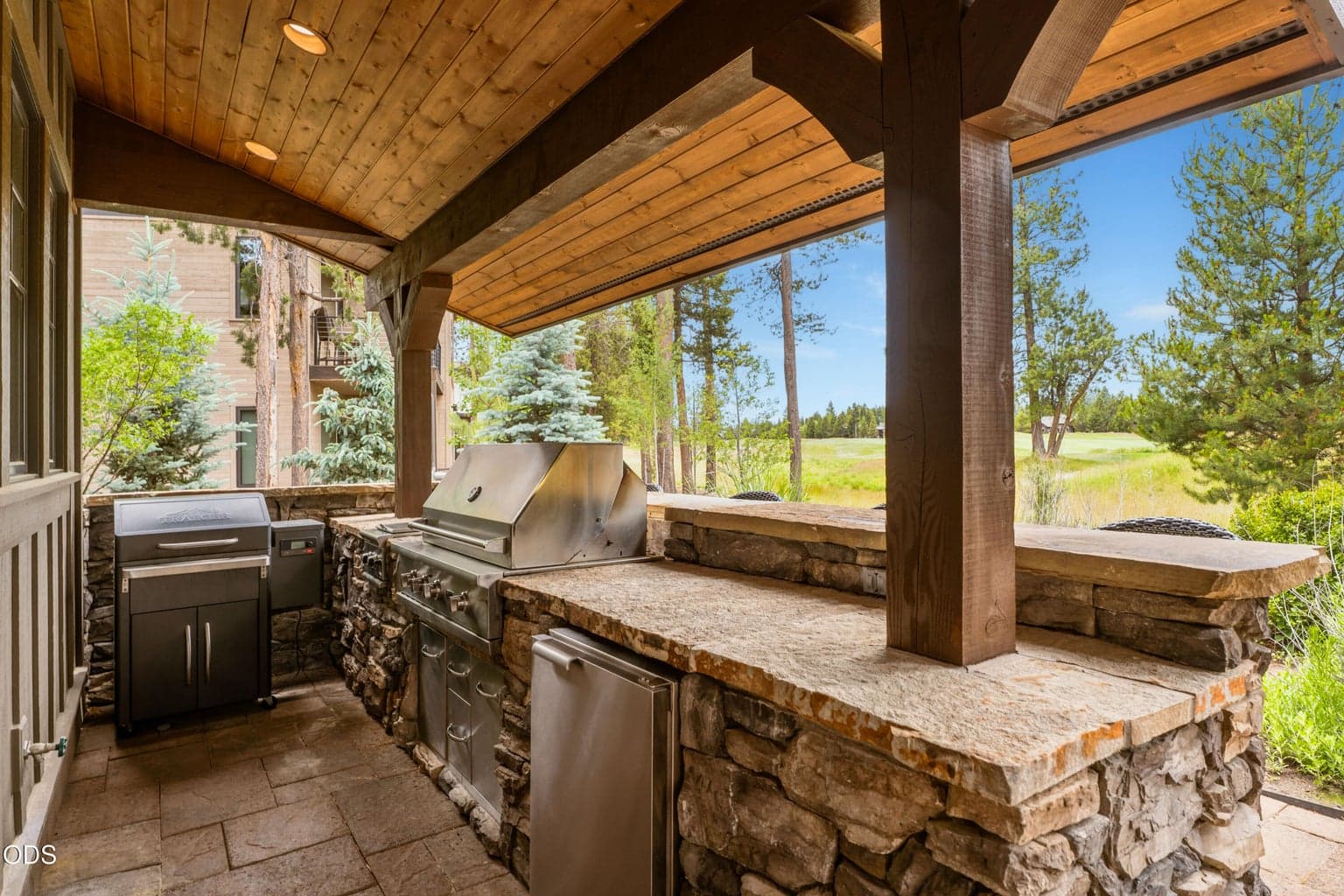 The covered outdoor living area features a built-in BBQ kitchen with stone accents and peaceful golf course views.