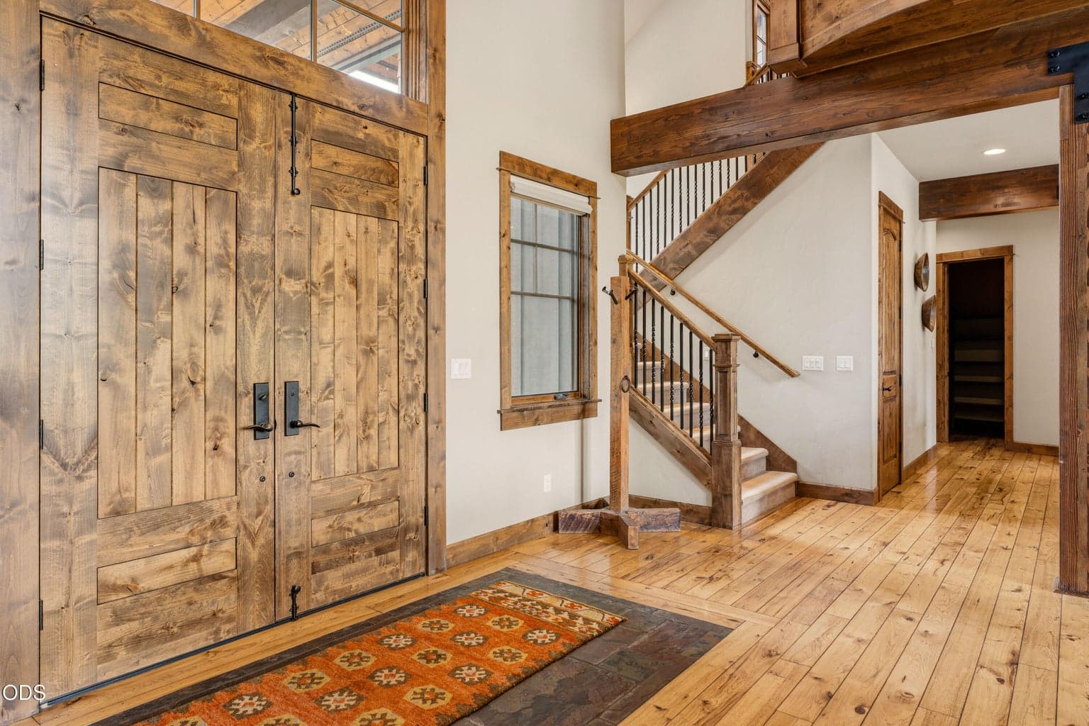 A dramatic two-story entry welcomes you with rustic double doors, exposed timber beams, and handcrafted wood and iron staircase details.