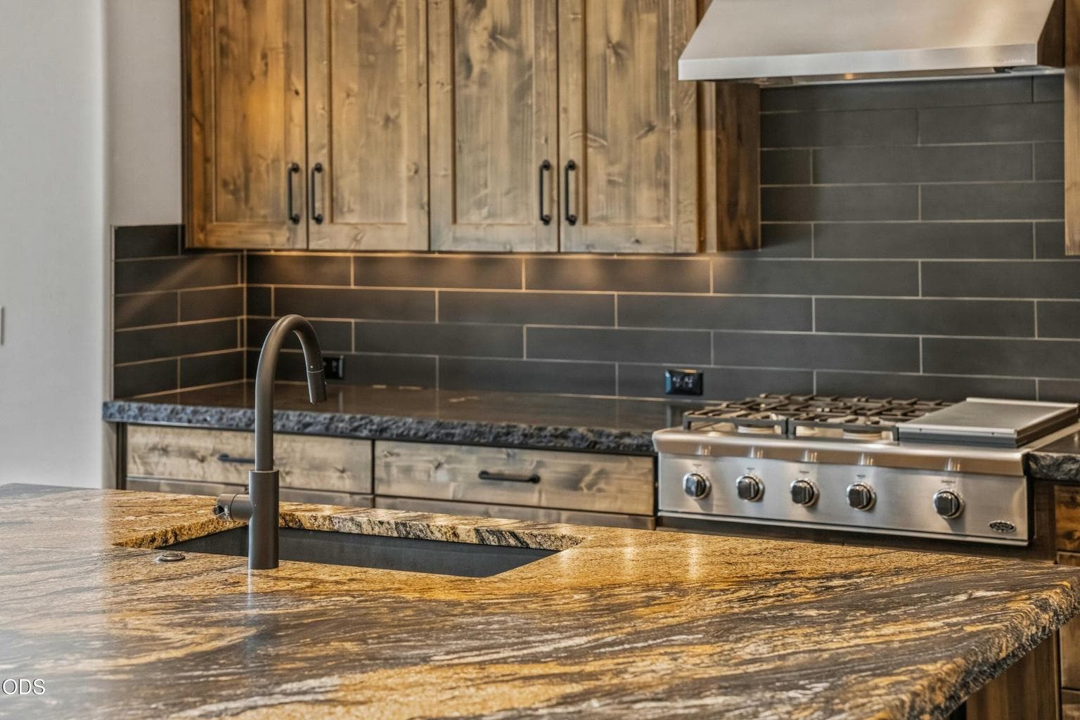Designer interiors can be curated, and here the details feel both elevated and grounded, with warm cabinetry, dark tile, and richly patterned counters creating a polished Northwest kitchen.