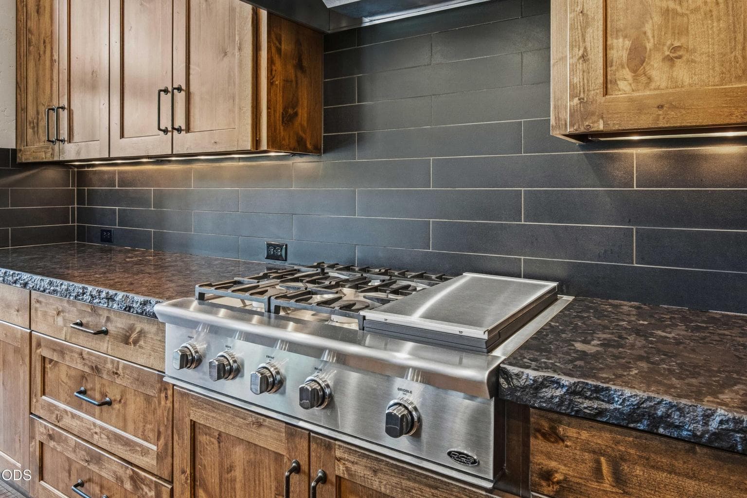 The kitchen pairs function and design with professional-style cooking, warm wood cabinetry, and a clean dark tile backdrop that complements the home’s contemporary High Desert character.