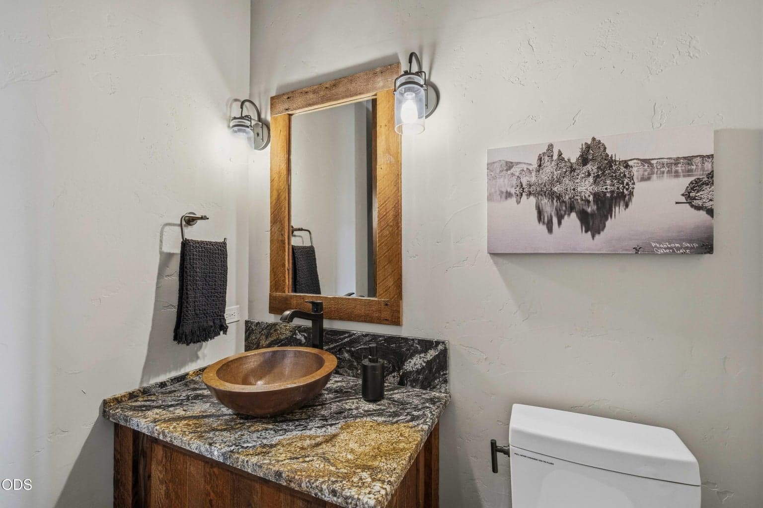 The powder bath continues the home’s refined rustic style, with a vessel sink, richly patterned counter, wood-framed mirror, and quiet Northwest detailing.