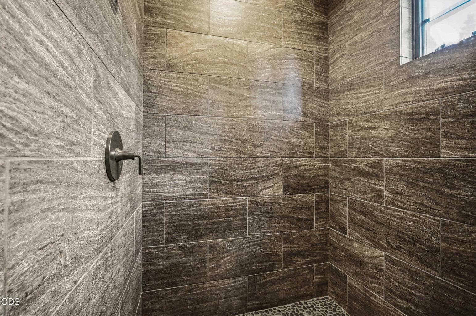 Stone-look tile, a clean glass enclosure, and natural textures give the primary shower a calm, refined Northwest retreat quality.