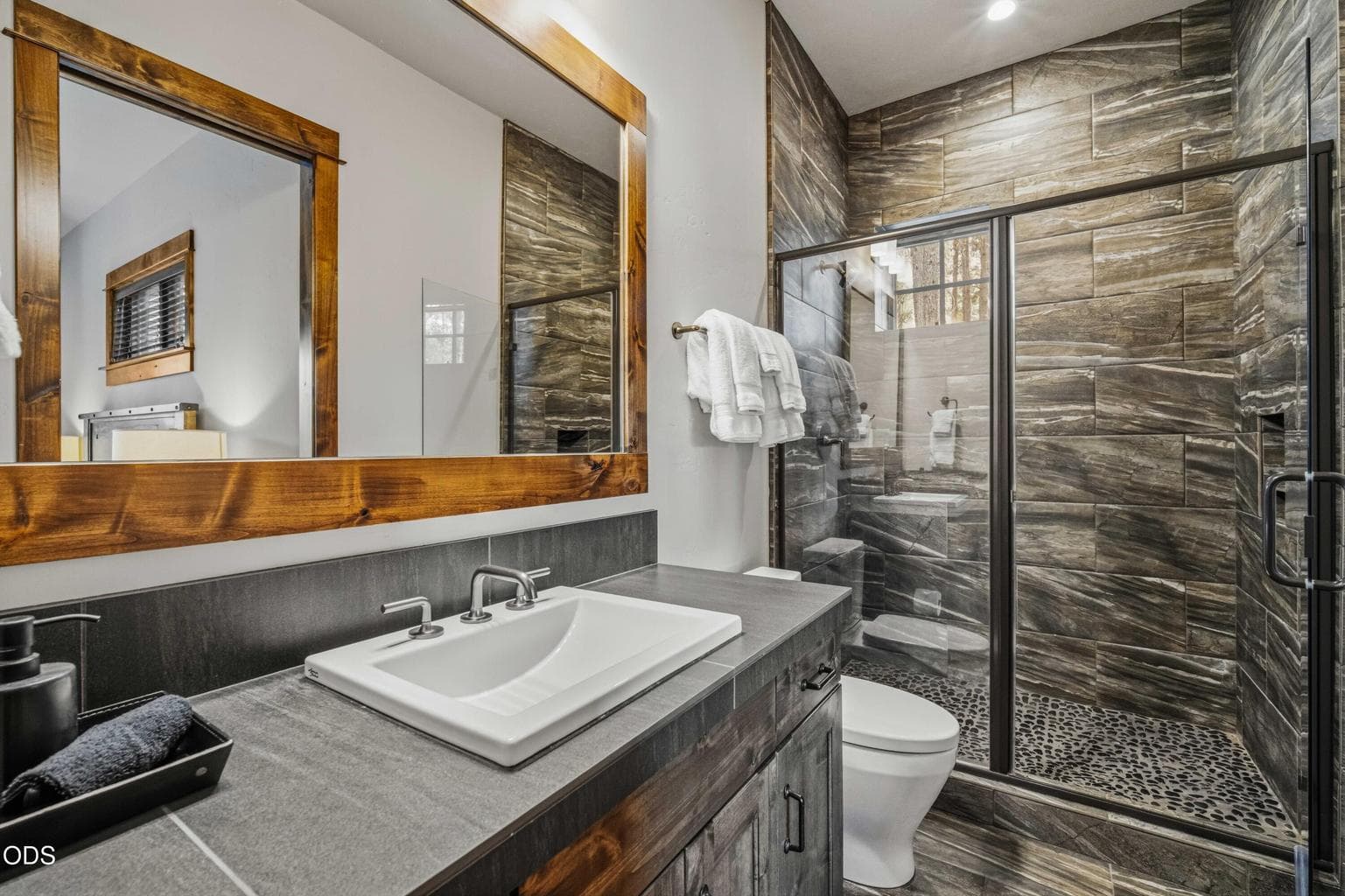 The guest bath continues the home’s cohesive material palette, pairing warm wood, clean lines, and refined finishes.
