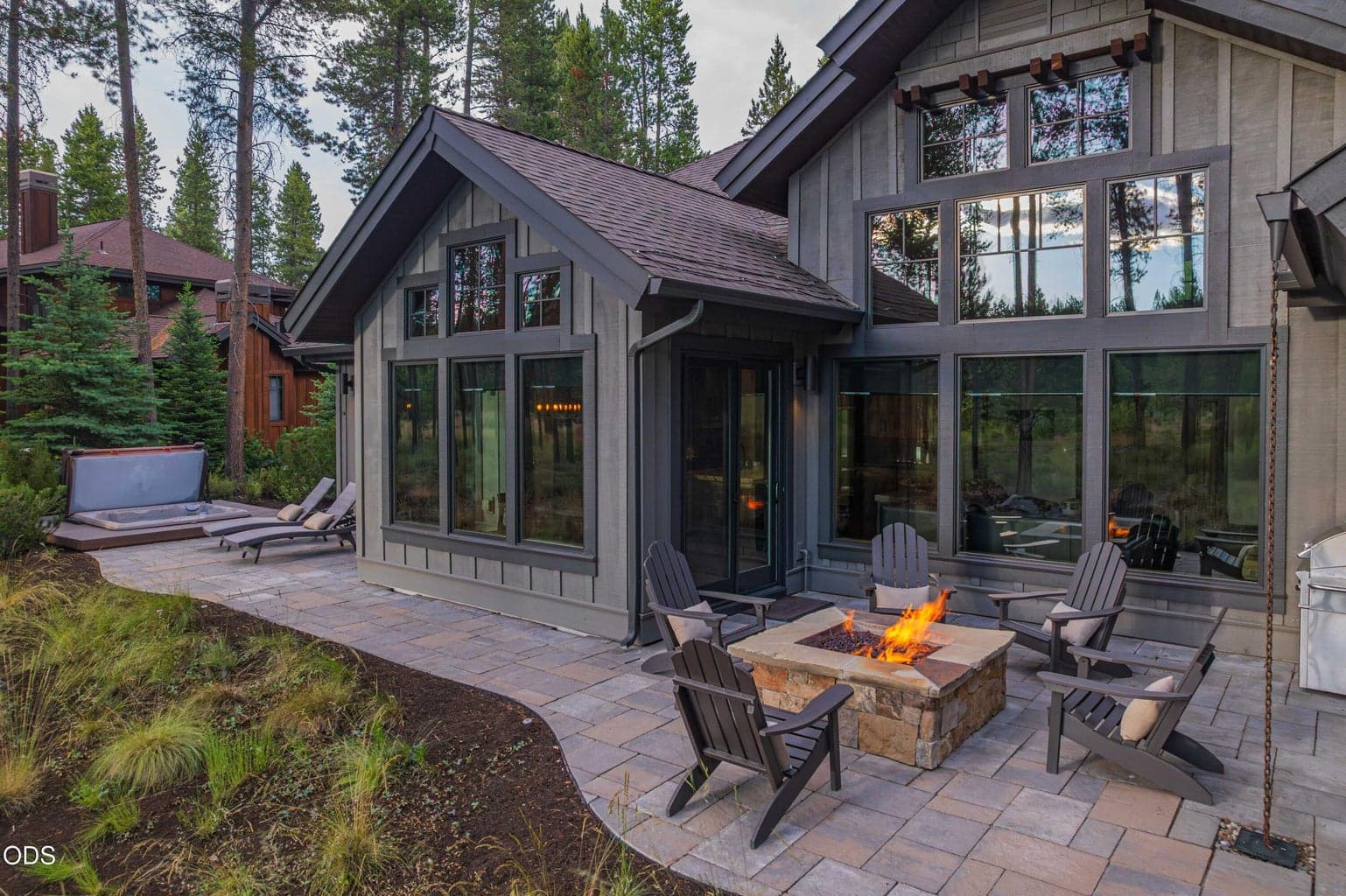 At dusk, the home glows beside the outdoor fire pit, highlighting the seamless connection between refined interiors, inviting outdoor spaces, and the natural landscape.