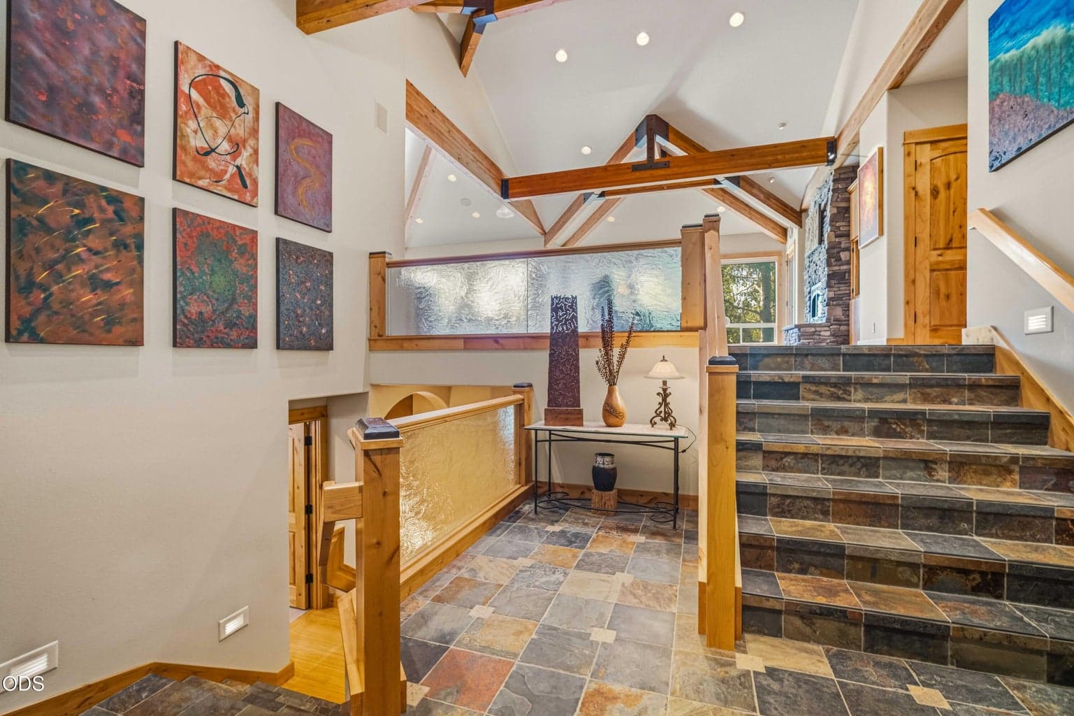 The central entry landing reveals the home’s practical split-level design, with only short stair runs leading to the primary living level and spacious lower level. Exposed beams and slate flooring add architectural distinction.