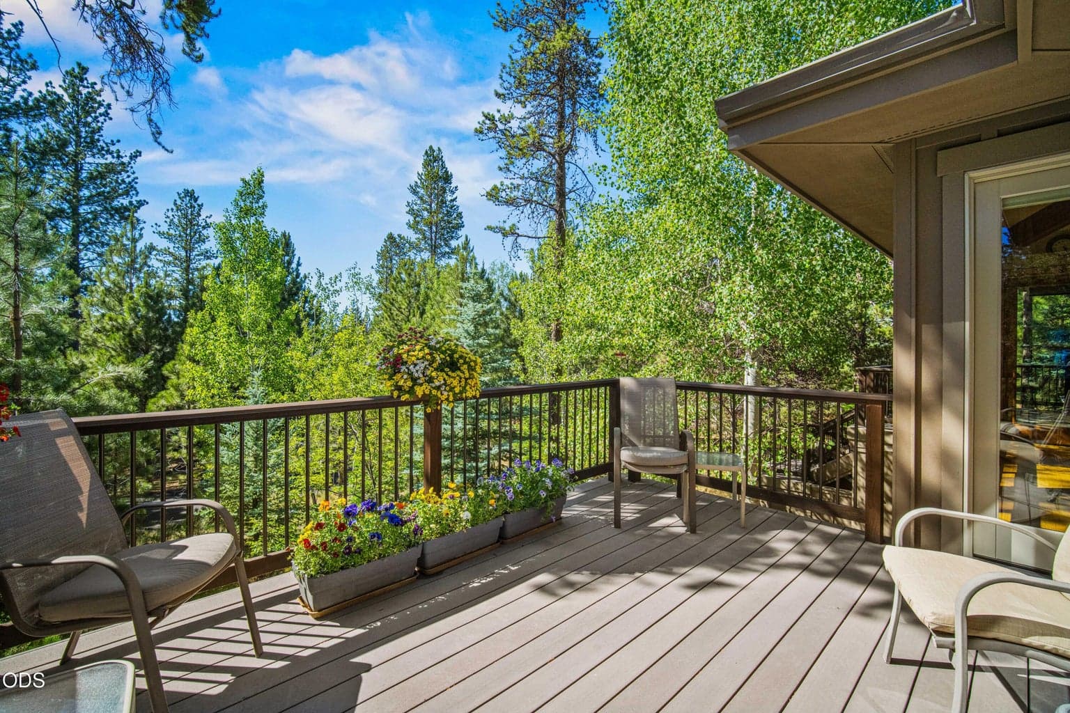 A second view shows how the dining-area deck wraps around the home toward the kitchen, creating a connected outdoor route and multiple seating areas. The elevated position captures layered forest views and the home’s orientation toward Mt. Bachelor.
