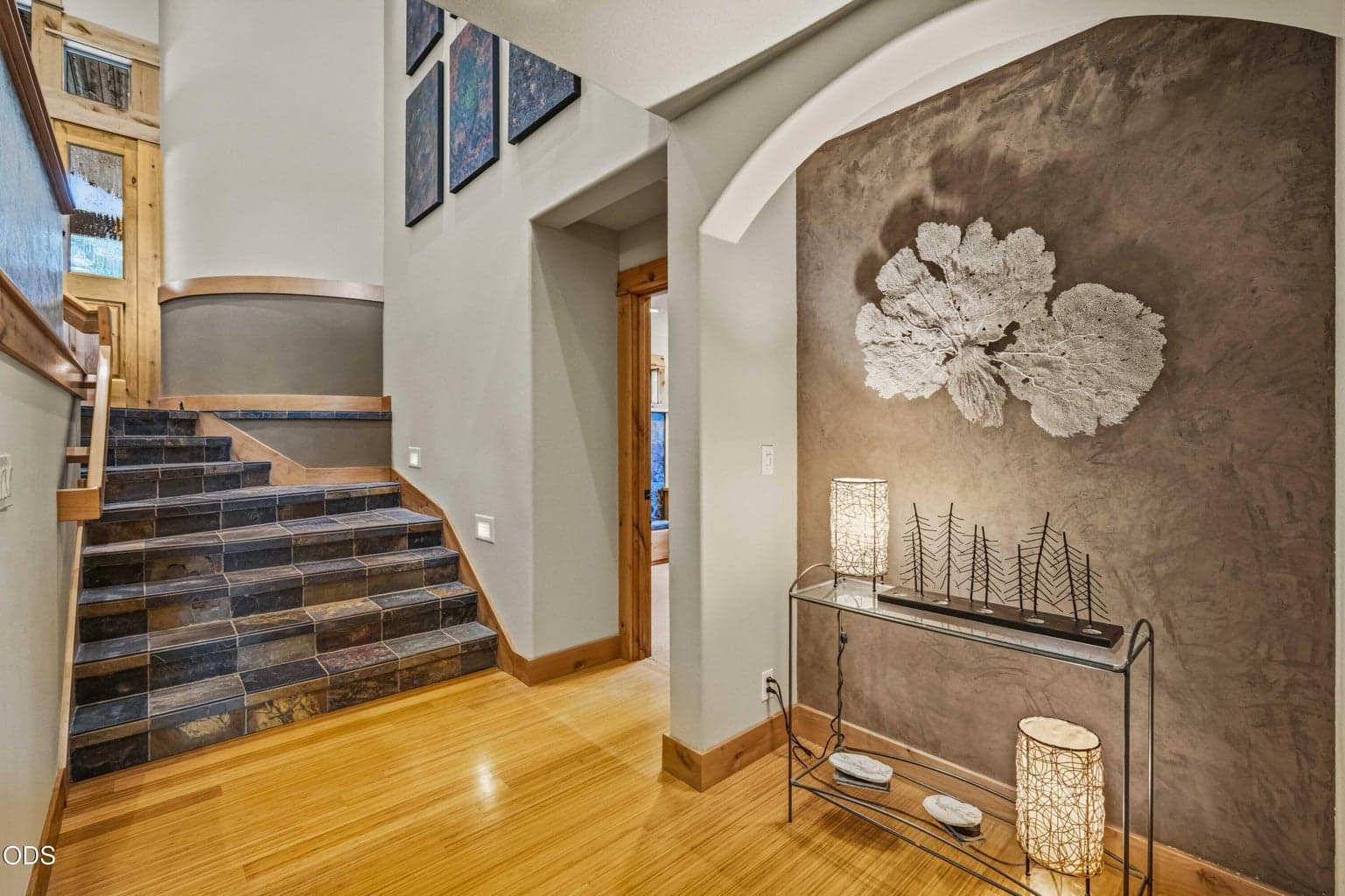 The lower-level hall continues the home’s artistic character with bamboo flooring, architectural niches and a dramatic textured art wall leading toward the library, bedrooms and wine cellar.