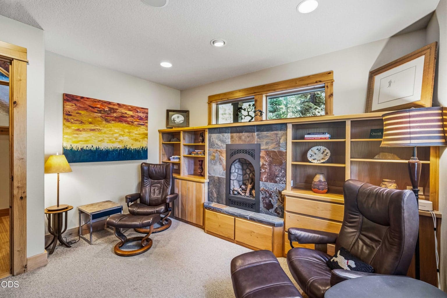A second angle shows the library’s comfortable proportions, built-in shelving, stone-and-slate fireplace surround and two distinct seating areas overlooking the trees.