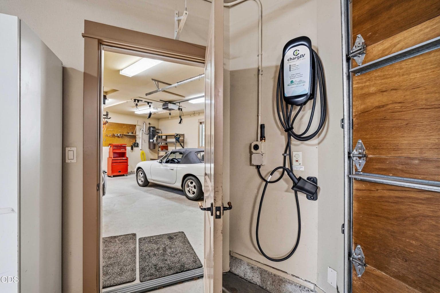 A dedicated electric vehicle charging station adds modern convenience within the three-car garage, positioned near the connection between the primary garage and workshop bay.
