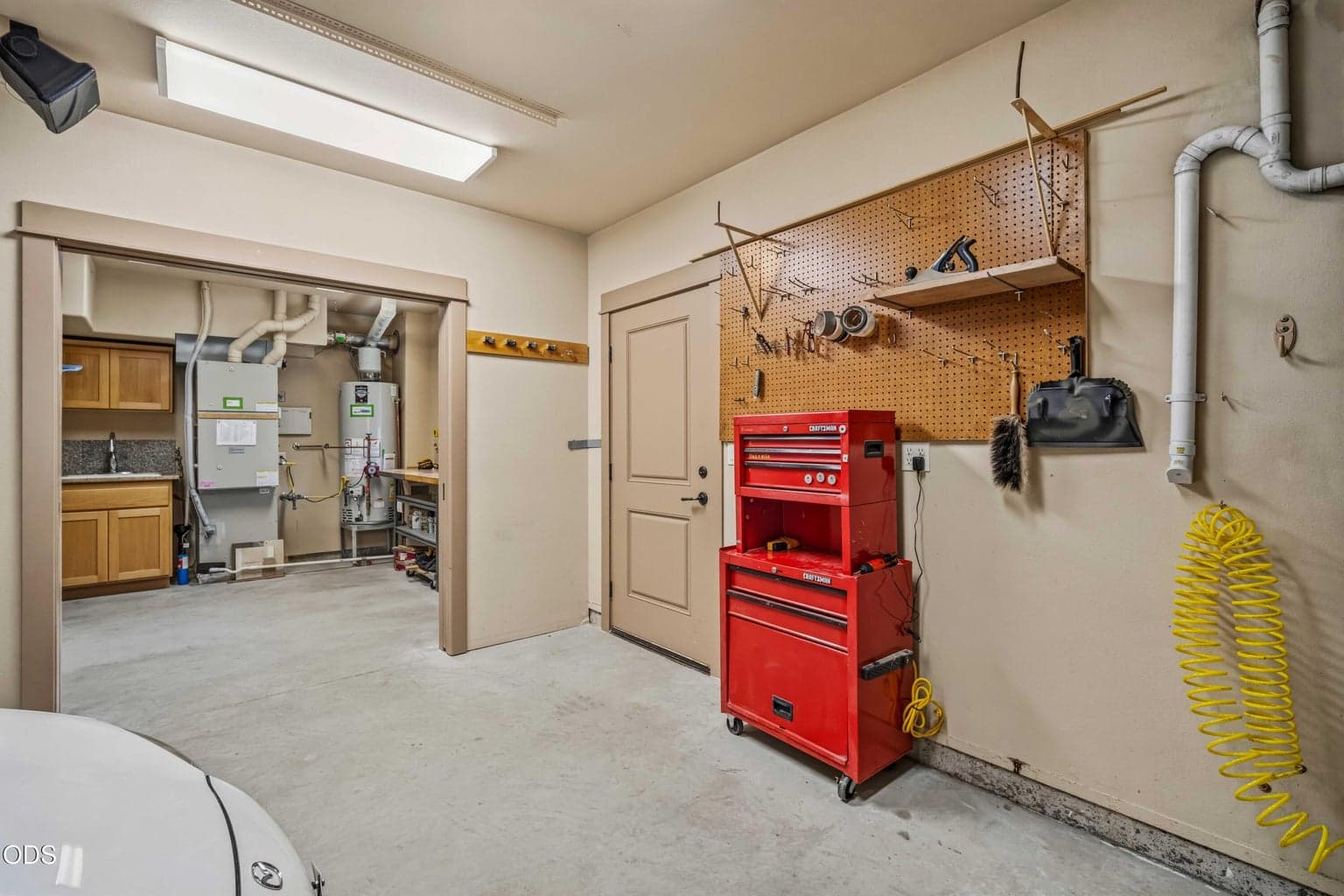 The workshop connects directly to a separate utility area with cabinetry, sink, mechanical equipment and additional work surfaces, creating an unusually functional support space.