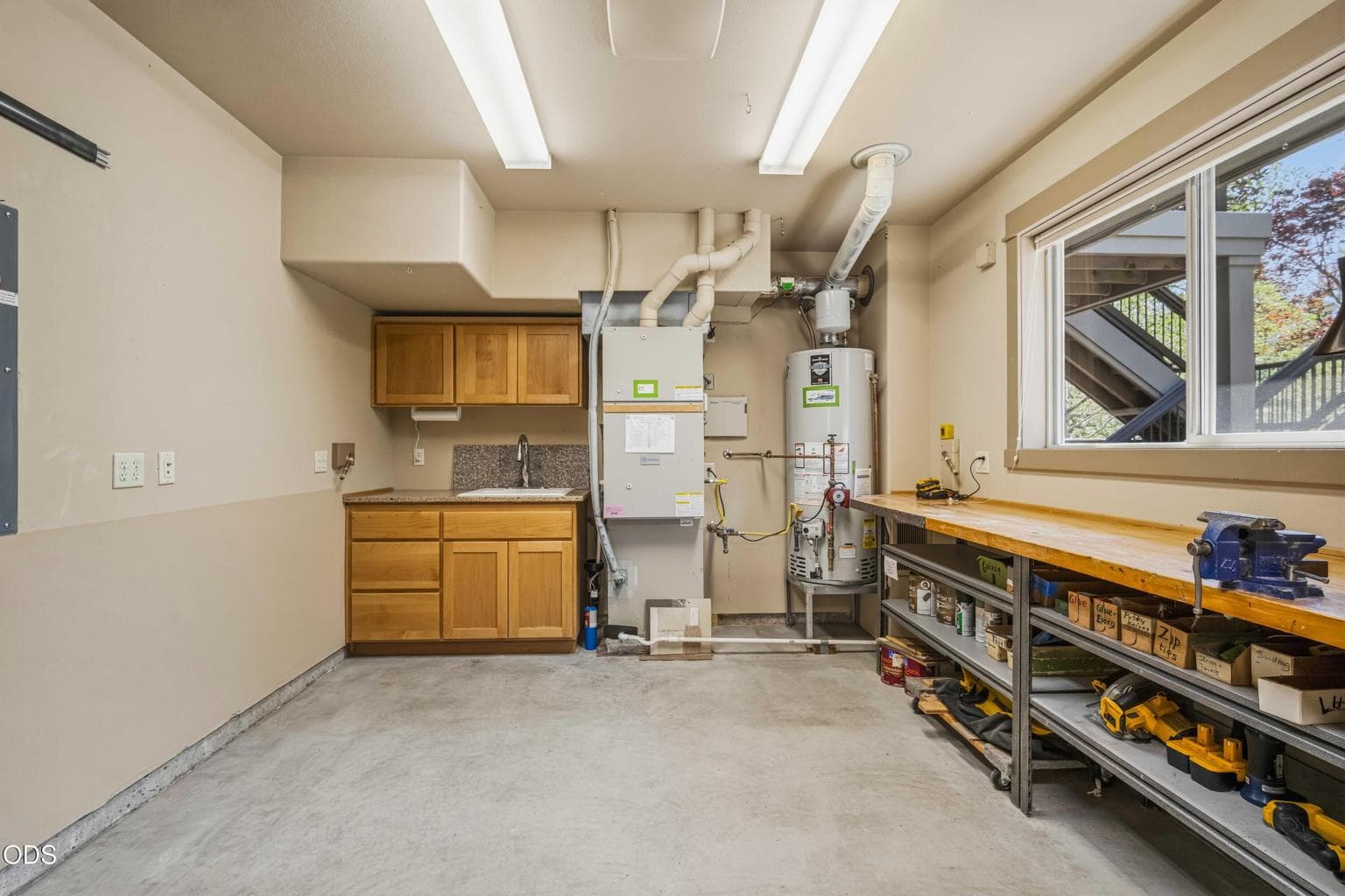 Located beyond the garage, the dedicated workshop includes a long workbench, vise, cabinetry, utility sink, bright lighting and a large window overlooking the forest.