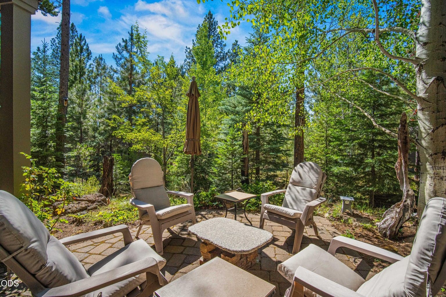 A secluded lower patio is nestled directly into the landscape, offering an intimate outdoor conversation area surrounded by mature evergreens, native rock and filtered sunlight.