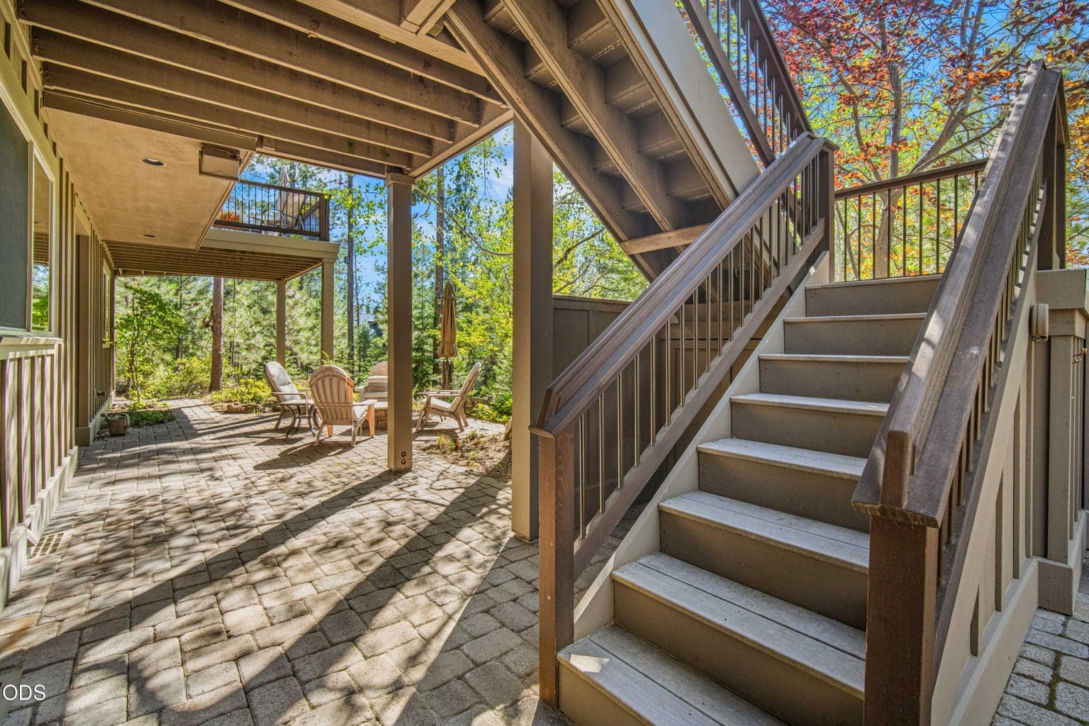 Covered outdoor space beneath the upper deck connects the lower patio, hot tub and forest seating areas, creating multiple protected outdoor zones linked by substantial exterior stairs.