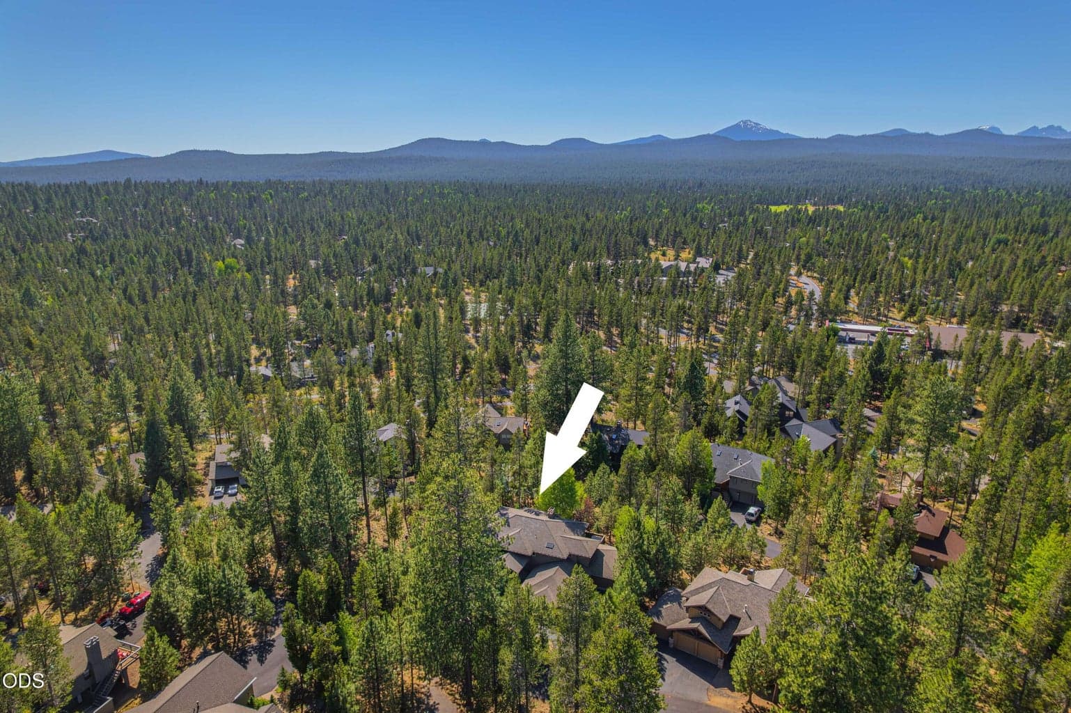 A broad aerial view places 21 Wallowa Loop within Sunriver’s forested landscape and shows its orientation toward Mount Bachelor and the Central Oregon Cascades. The arrow identifies the property location.