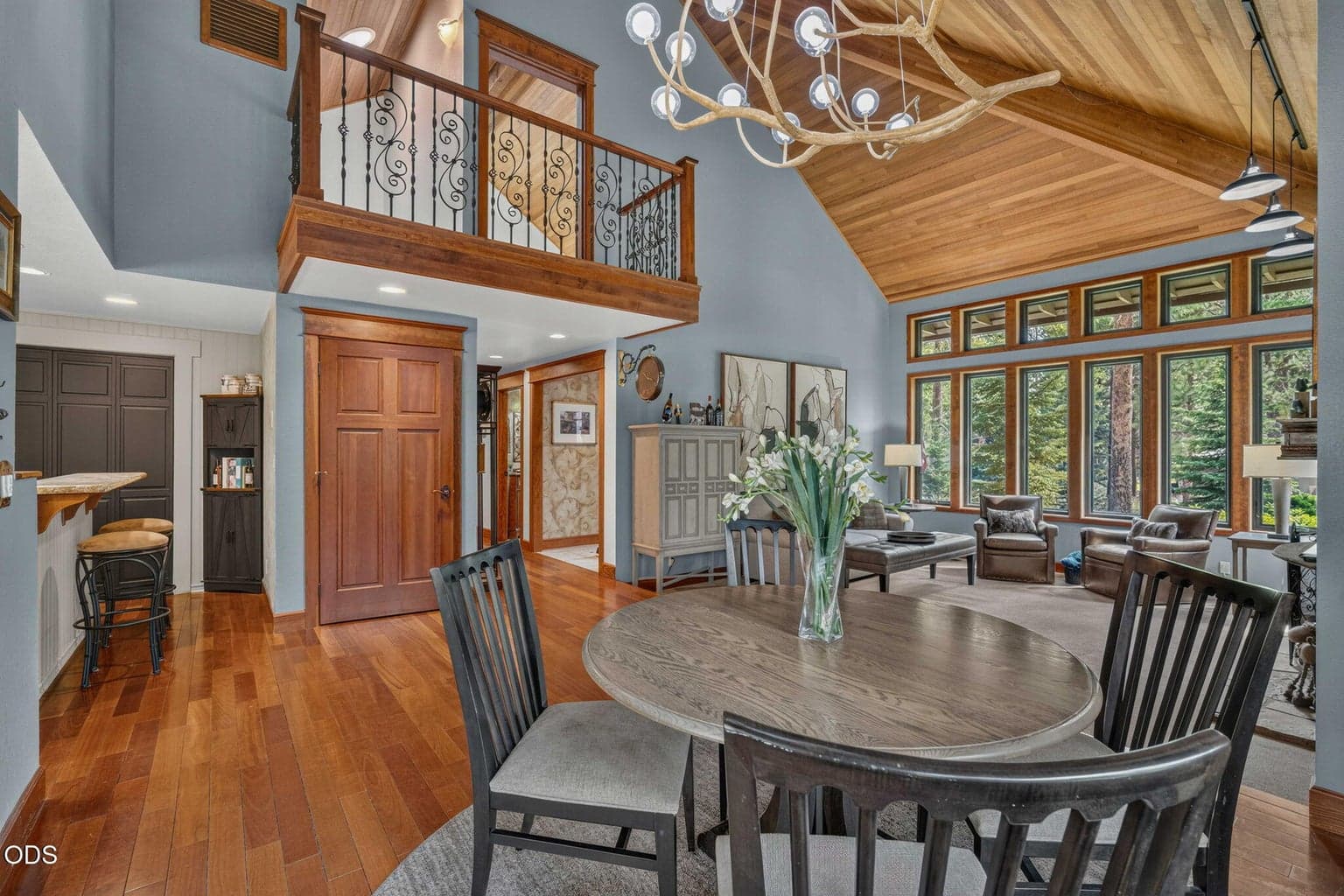 Elegant dining and living space with vaulted cedar ceilings, iron railed loft above to upper suite and abundant natural light filters in.