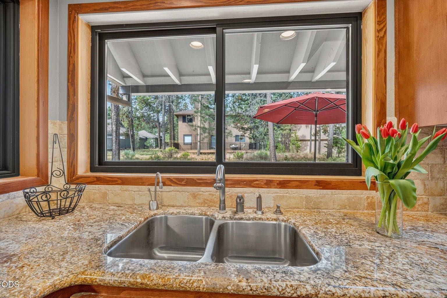 Dual basin sink with granite surround and scenic window overlooking backyard patio dining .