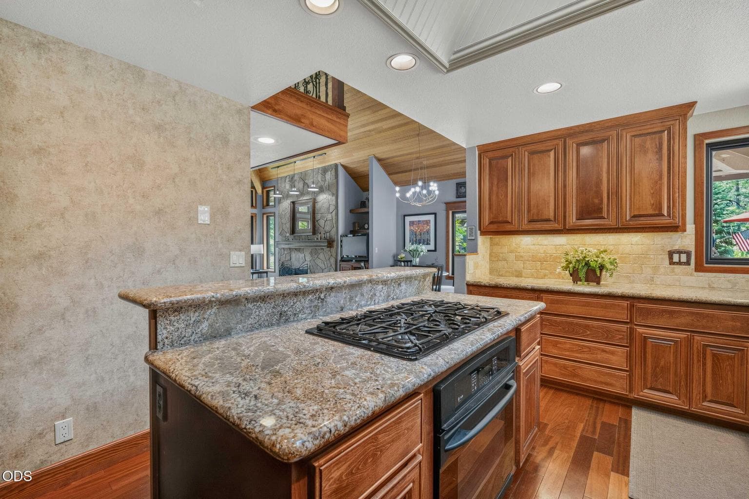 Chef’s kitchen connects to living area, showcasing granite, rich wood tones and natural light.