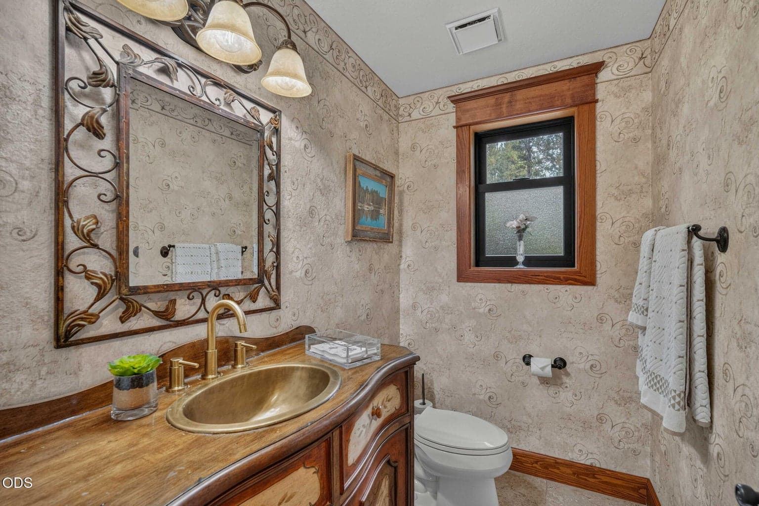 Elegant powder bath with gold basin, ornate mirror and warm wood accents.